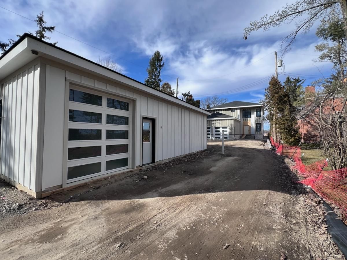 Modern white building with garage doors beside a dirt driveway under a cloudy blue sky