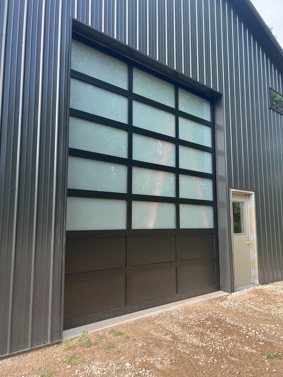 Dark corrugated metal building exterior with a large frosted windowed garage door and side door