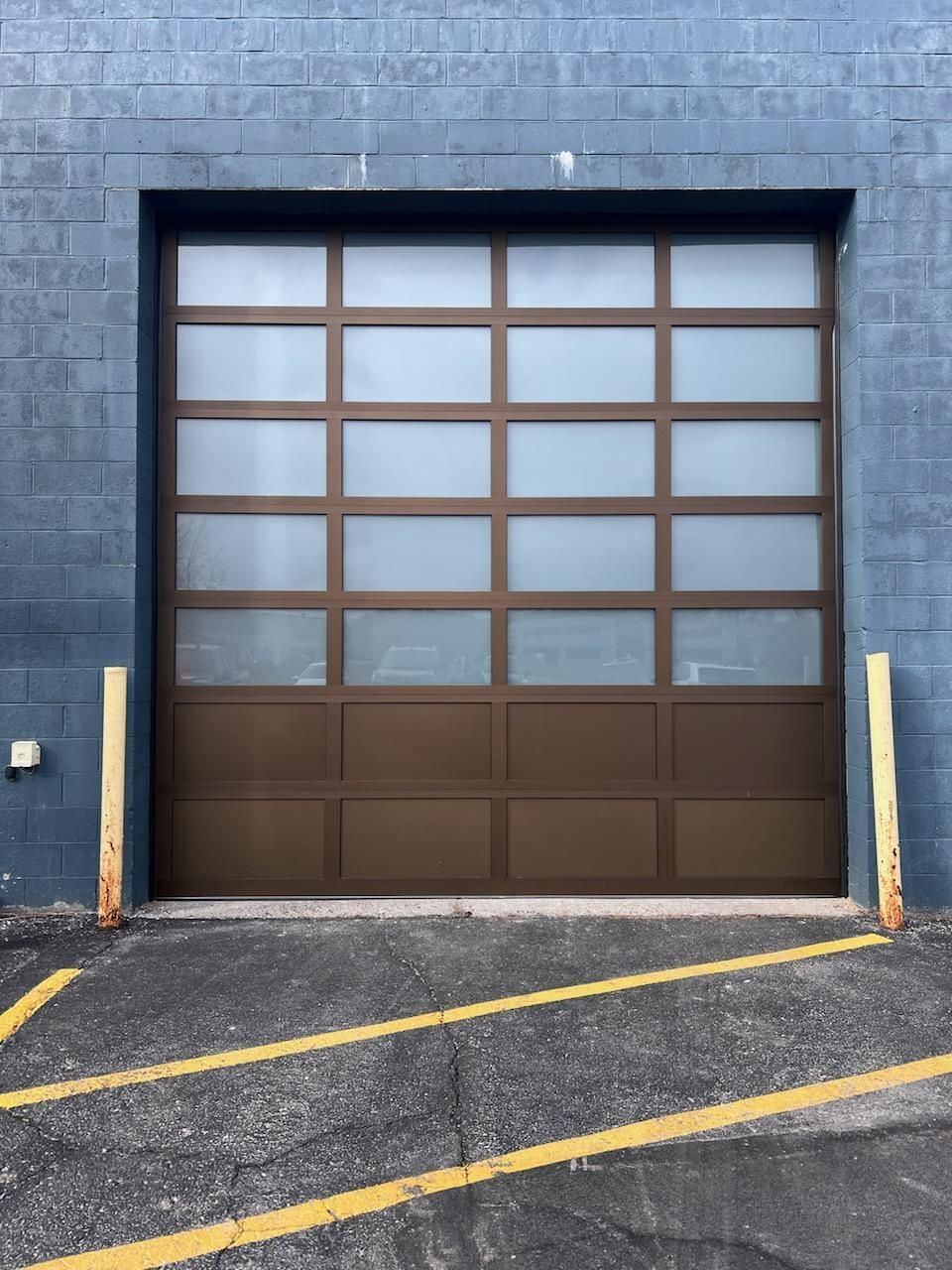 Blue industrial building with a brown garage door and yellow parking lines in front