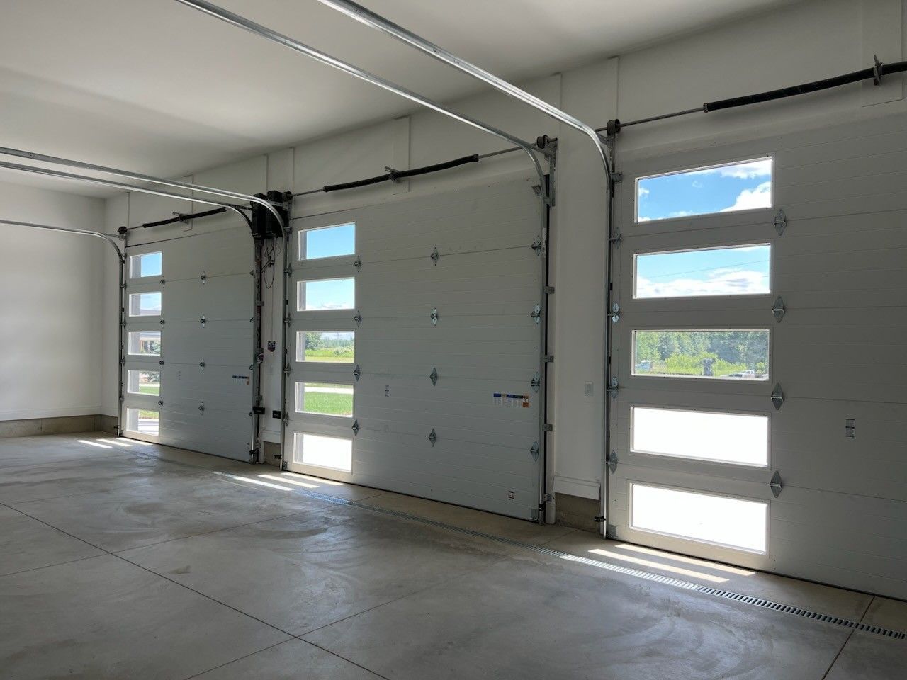 Empty garage interior with white sectional doors and narrow windows letting in daylight