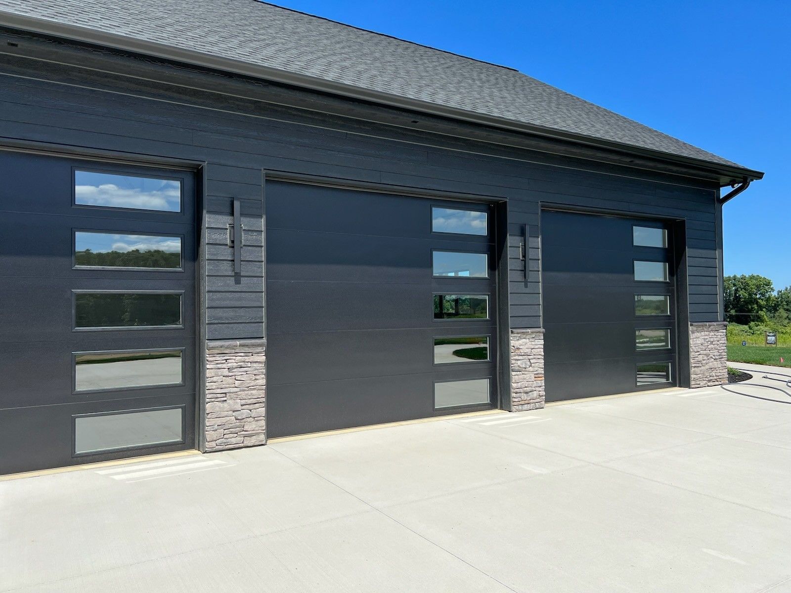 Modern gray garage with three glass-panel doors on a concrete driveway under a dark roof.