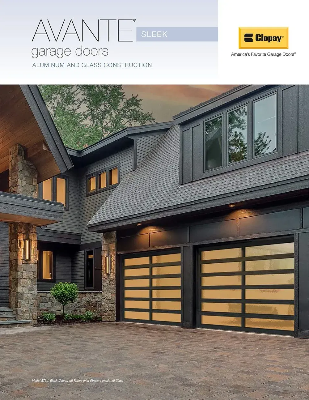 Modern gray house exterior with warm lit garage doors and stone driveway at dusk