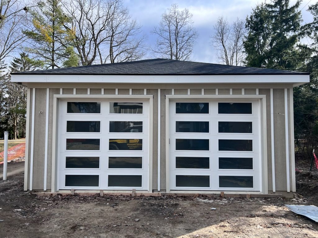 Two-car garage with white doors and beige siding under a dark roof, viewed from the front