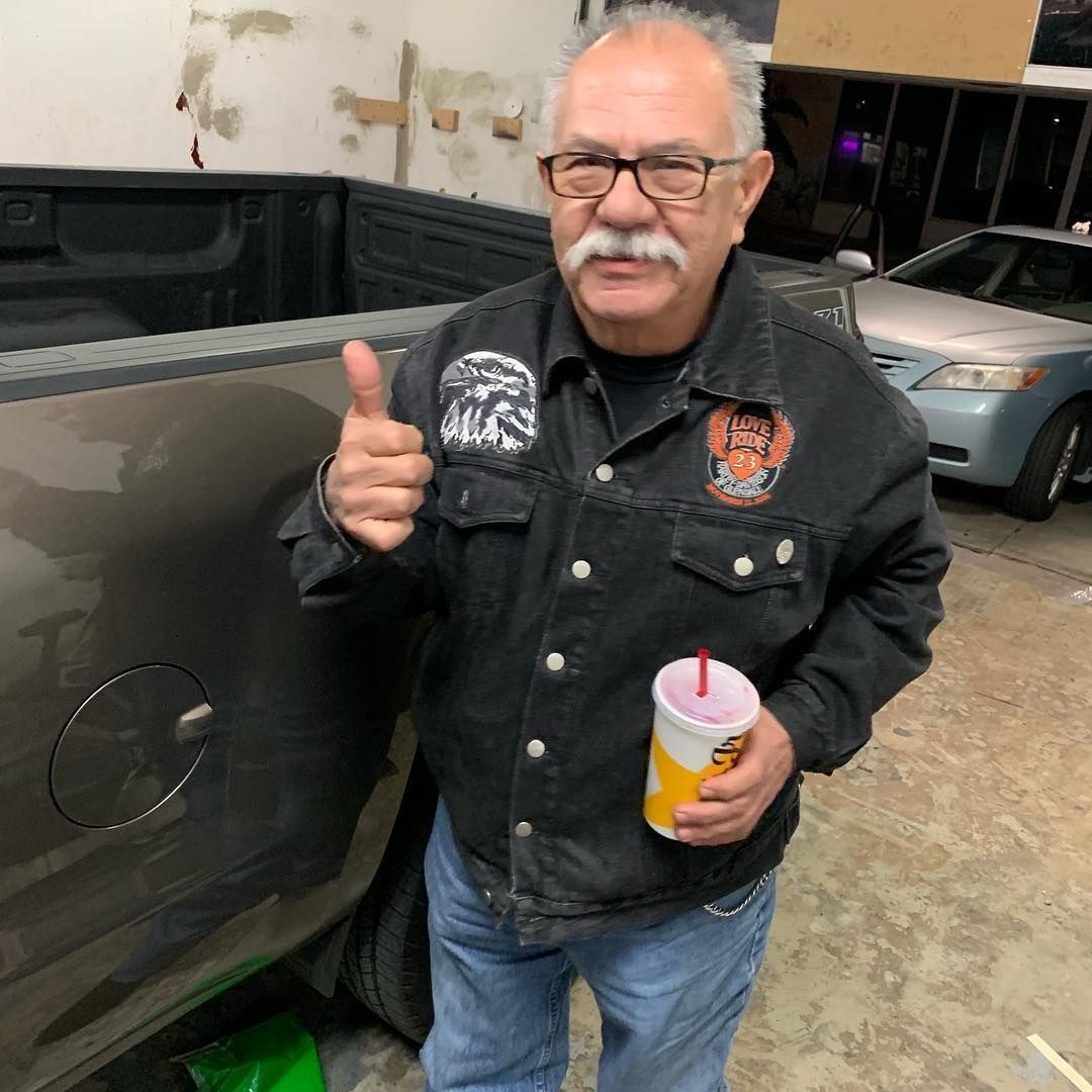 A man with a mustache and glasses is giving a thumbs up