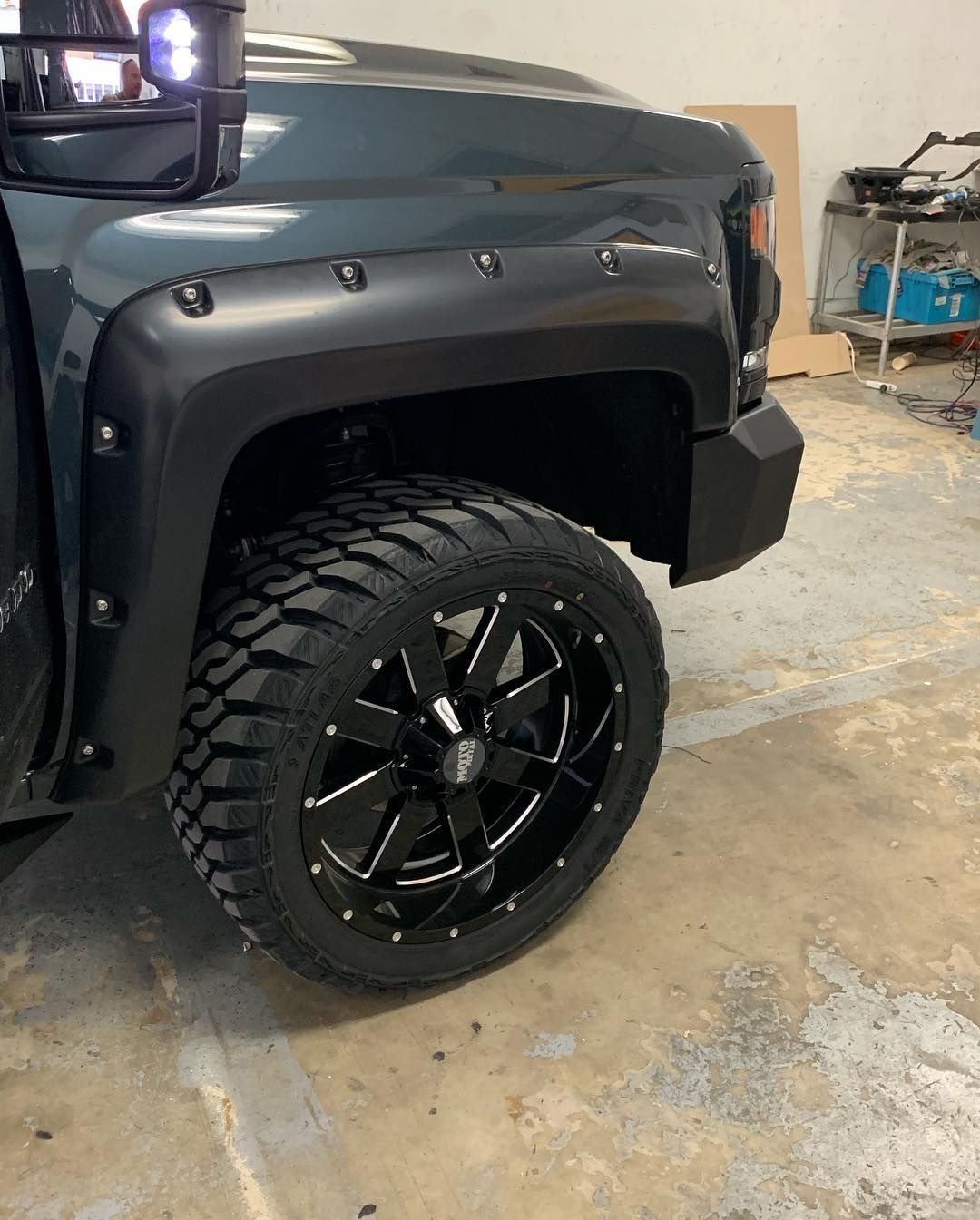 A black truck with black wheels and tires is parked in a garage.