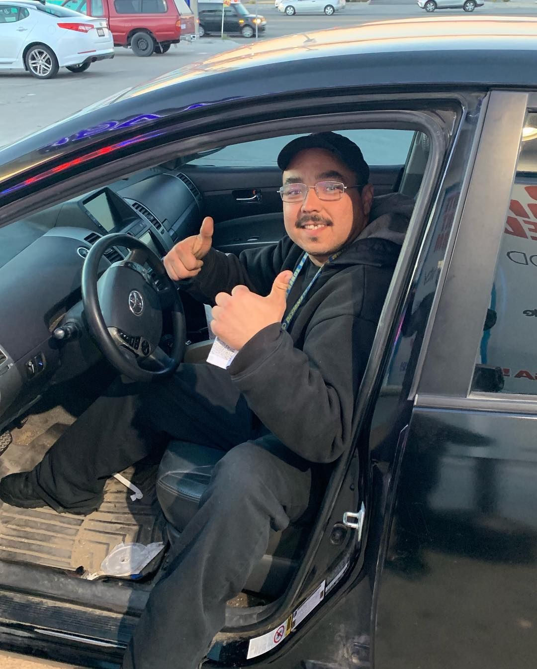 A man is sitting in the driver's seat of a car giving a thumbs up.