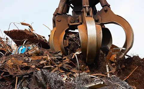 Excavator claw lifting scrap metal and debris in a junkyard