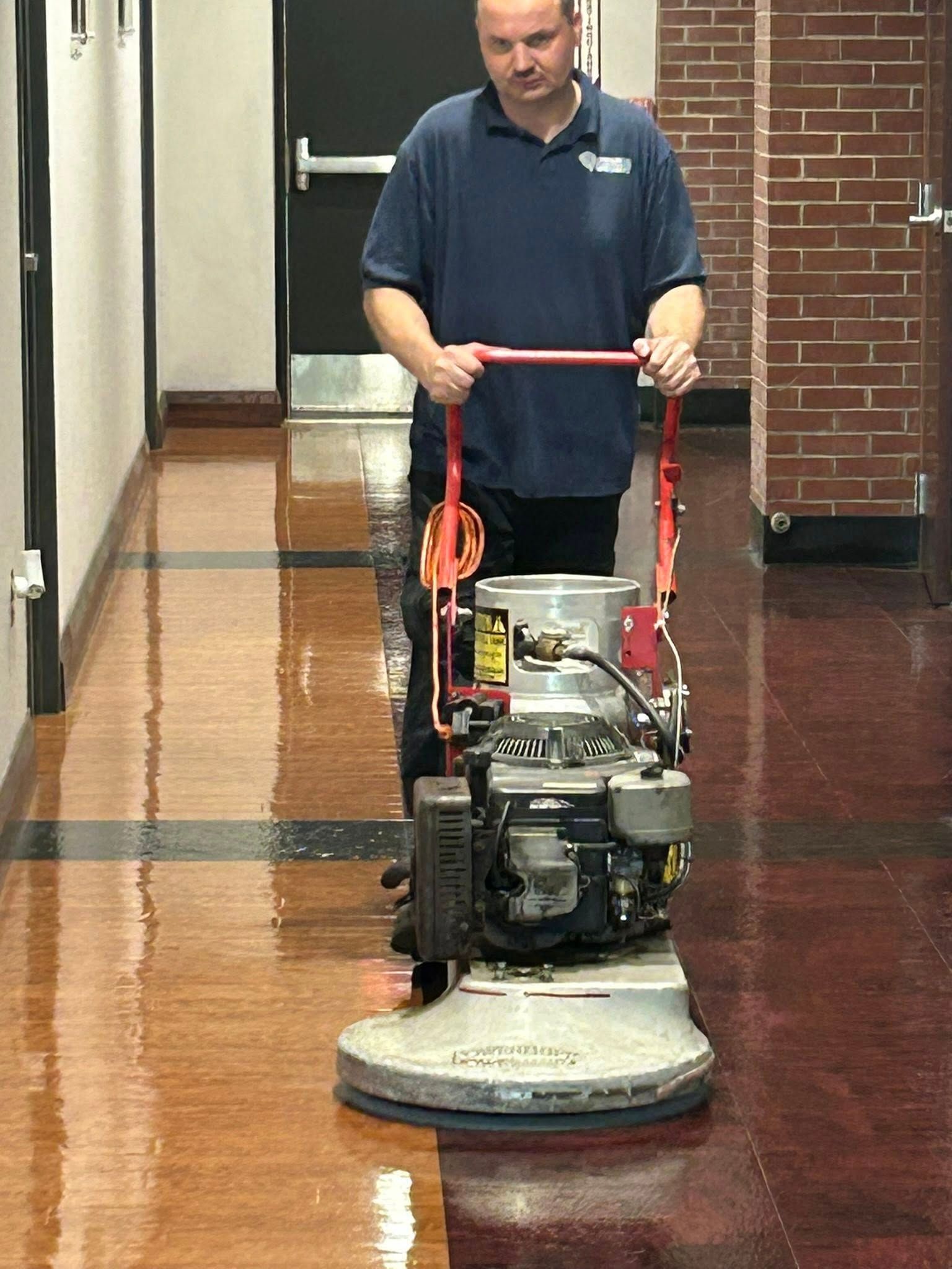 Man using a floor buffer on a shiny wooden hallway floor.