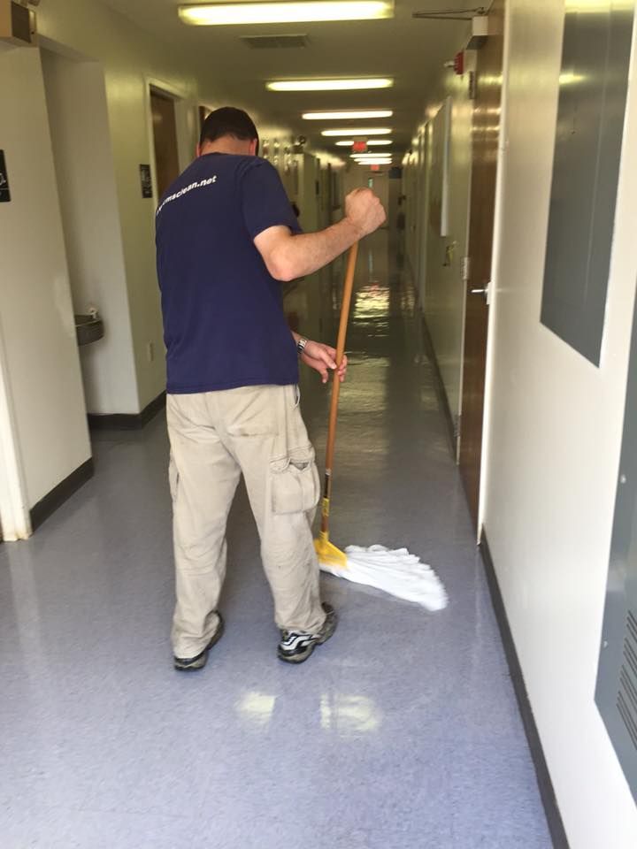 A man in a blue shirt cleans a hallway floor with a mop.