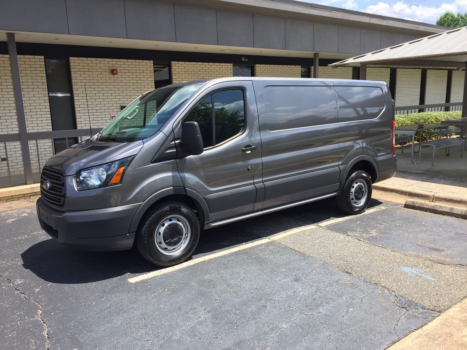 Gray cargo van parked outside a building, with tinted windows and visible headlights.