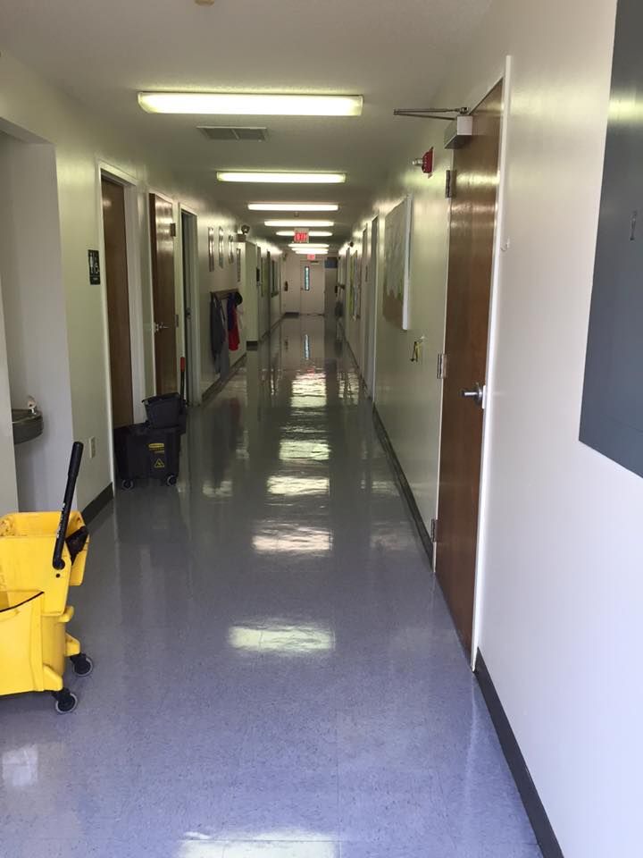 Man mopping a long hallway with light blue floor and white doors.