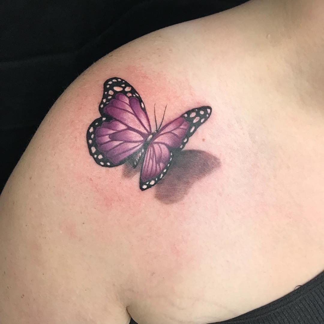 A woman has a purple butterfly tattoo on her shoulder.