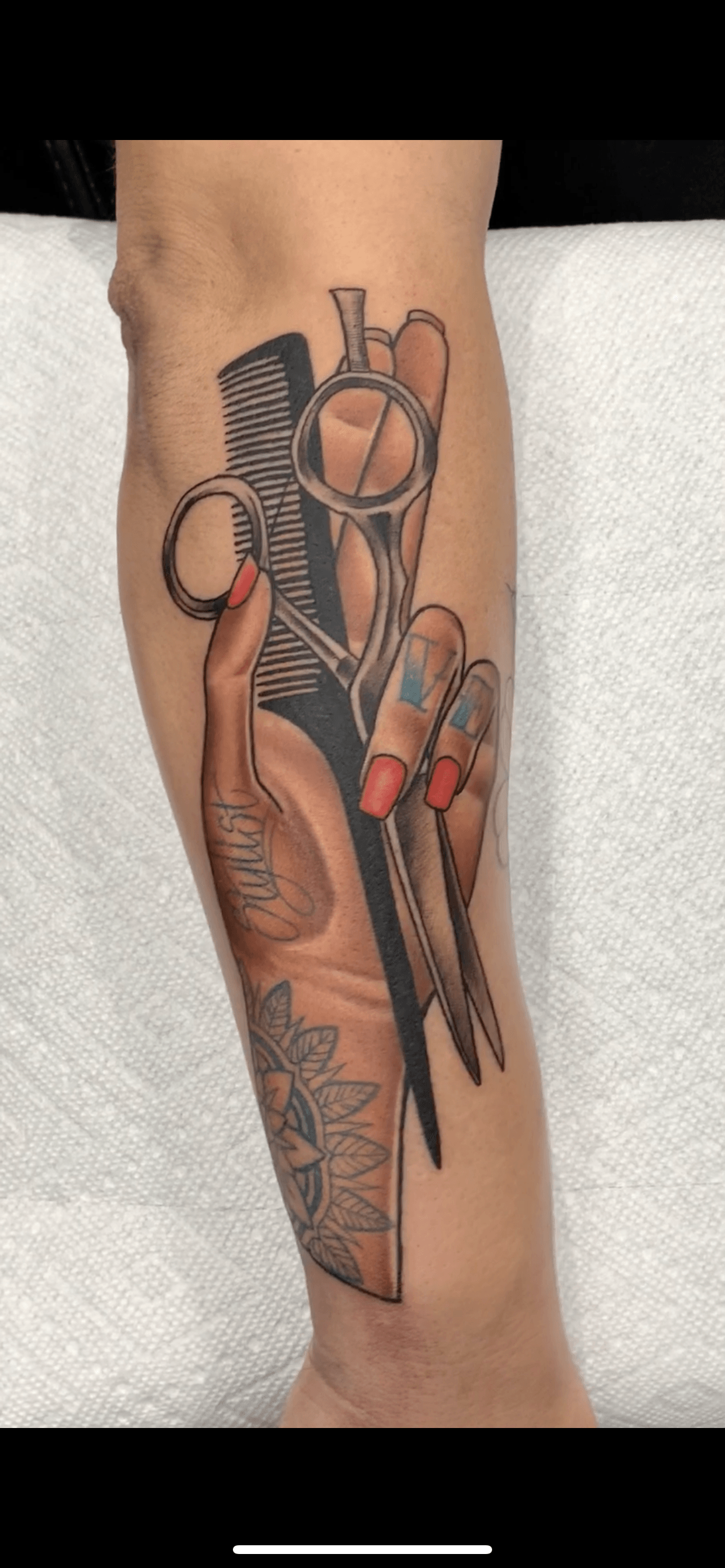A tattoo of a woman 's hand holding a pair of scissors and a comb.