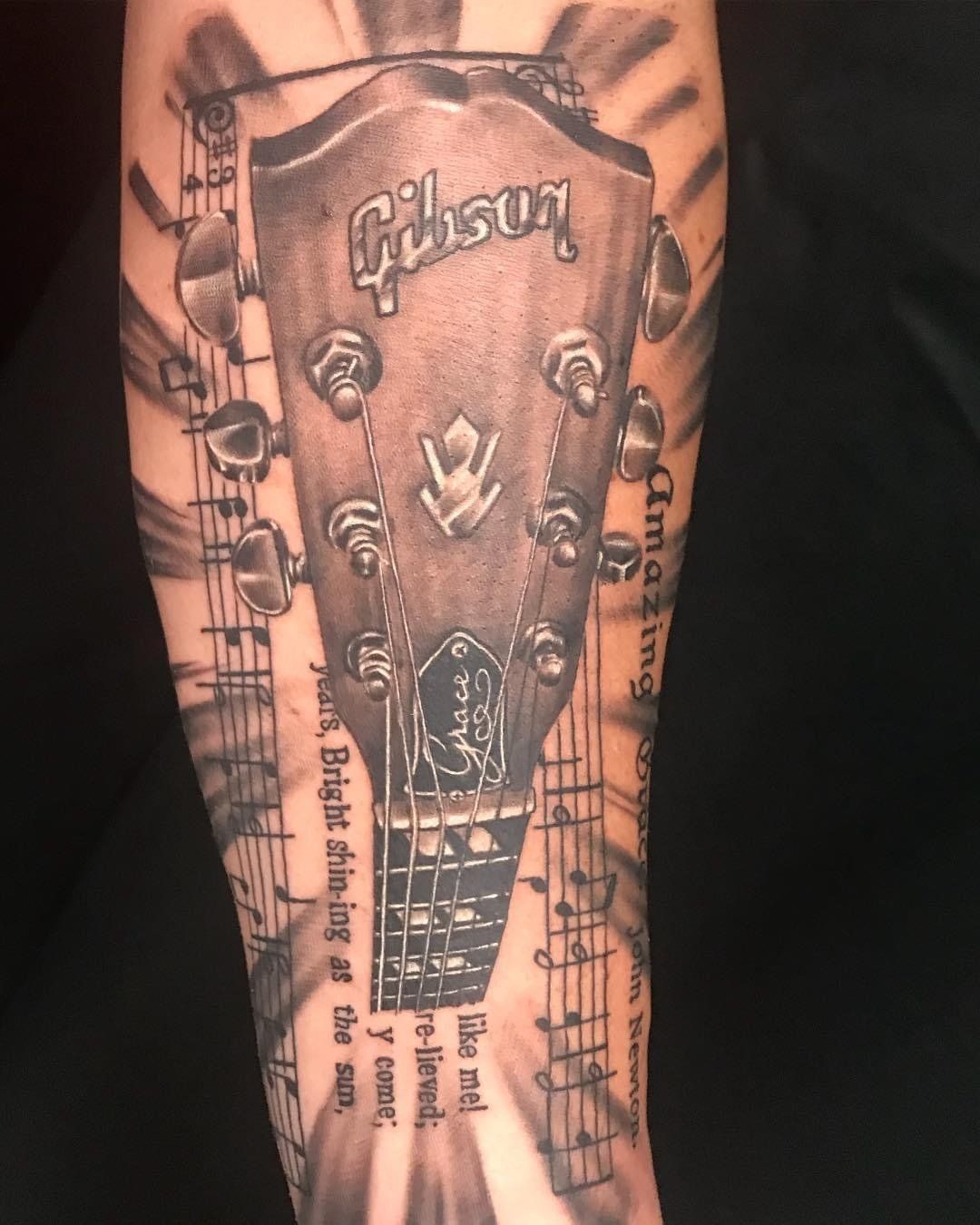 A black and white tattoo of a gibson guitar headstock