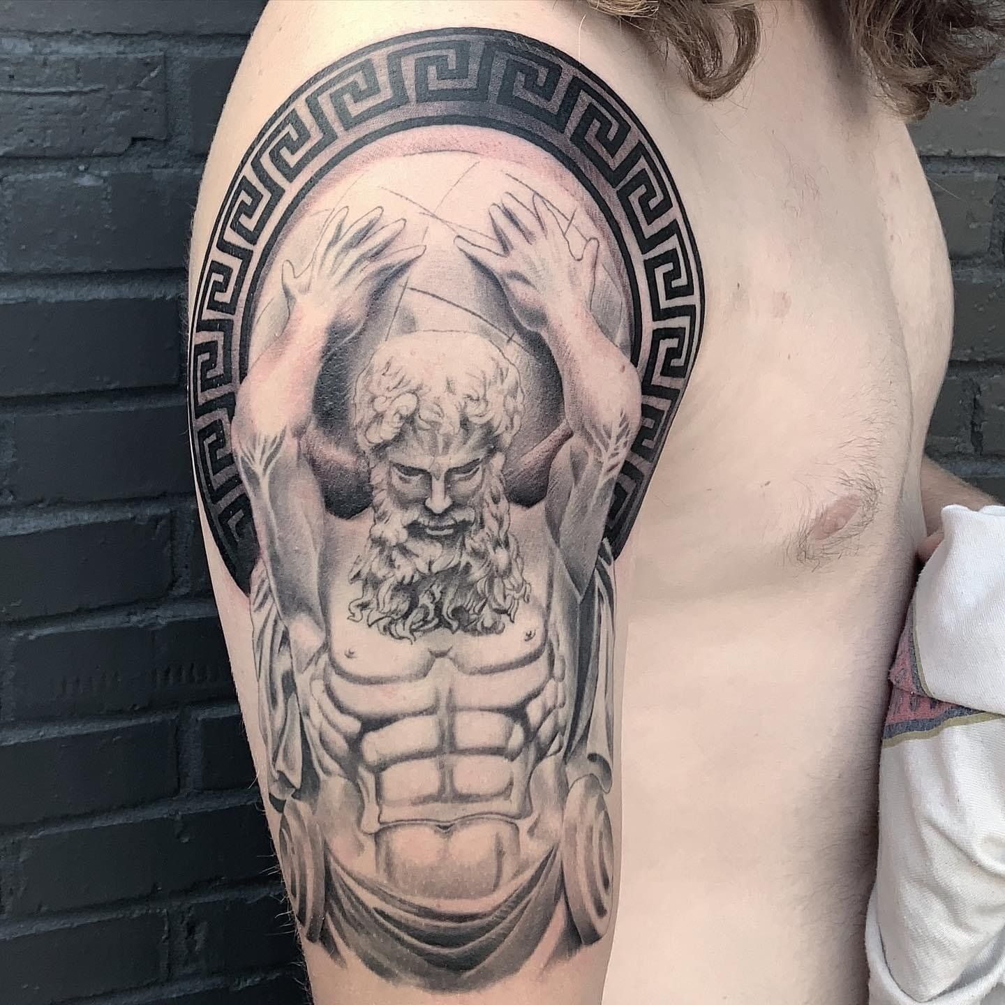 A man has a tattoo of a statue on his arm.