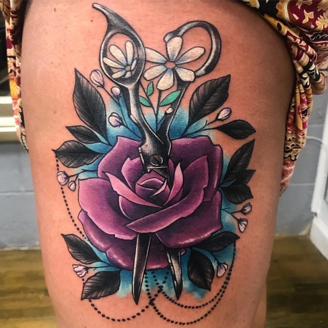 A tattoo of a pair of scissors cutting a purple rose