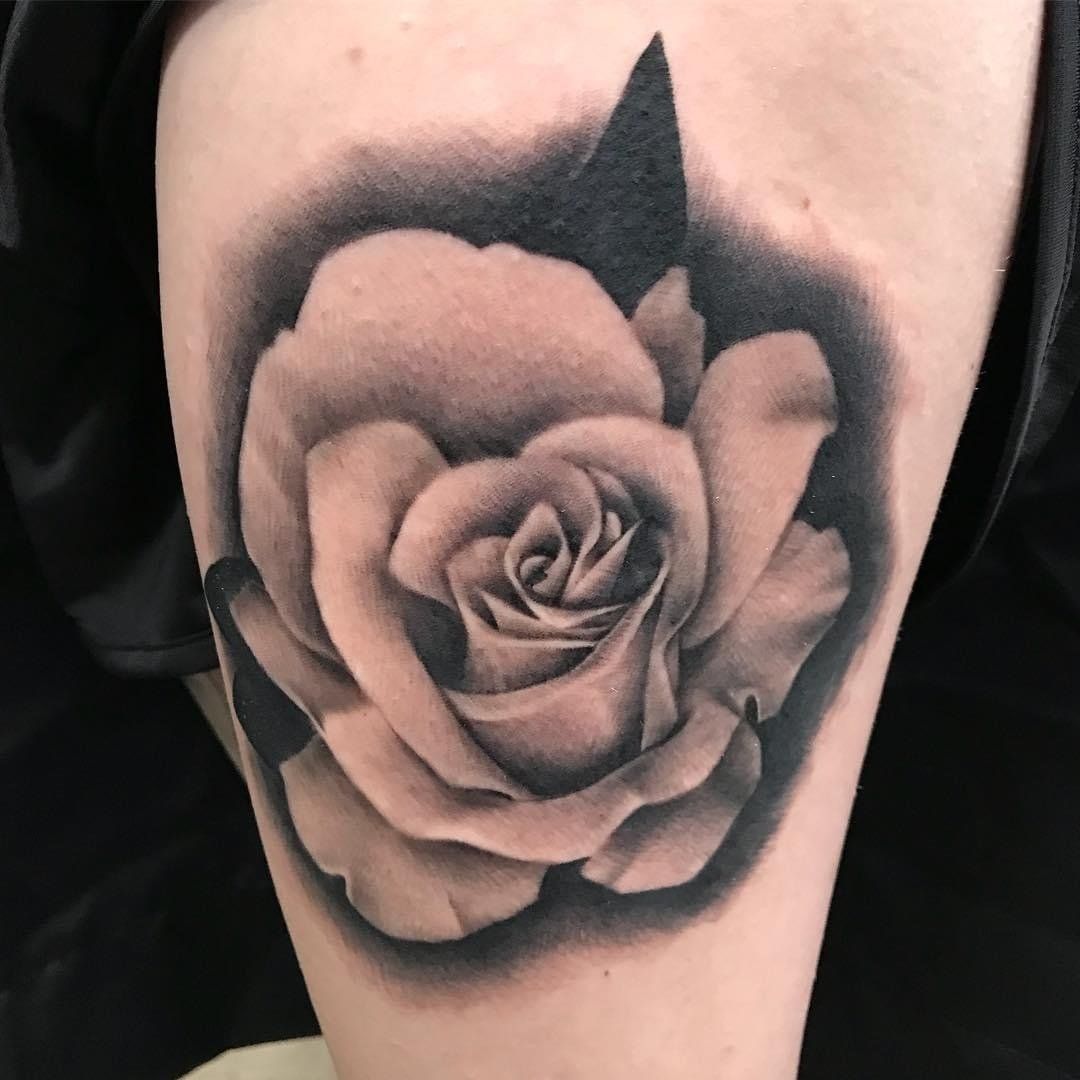 A black and white tattoo of a rose on a person 's leg.
