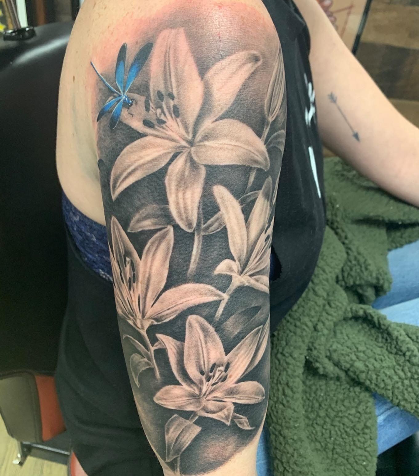 A woman has a tattoo of flowers and a dragonfly on her arm.