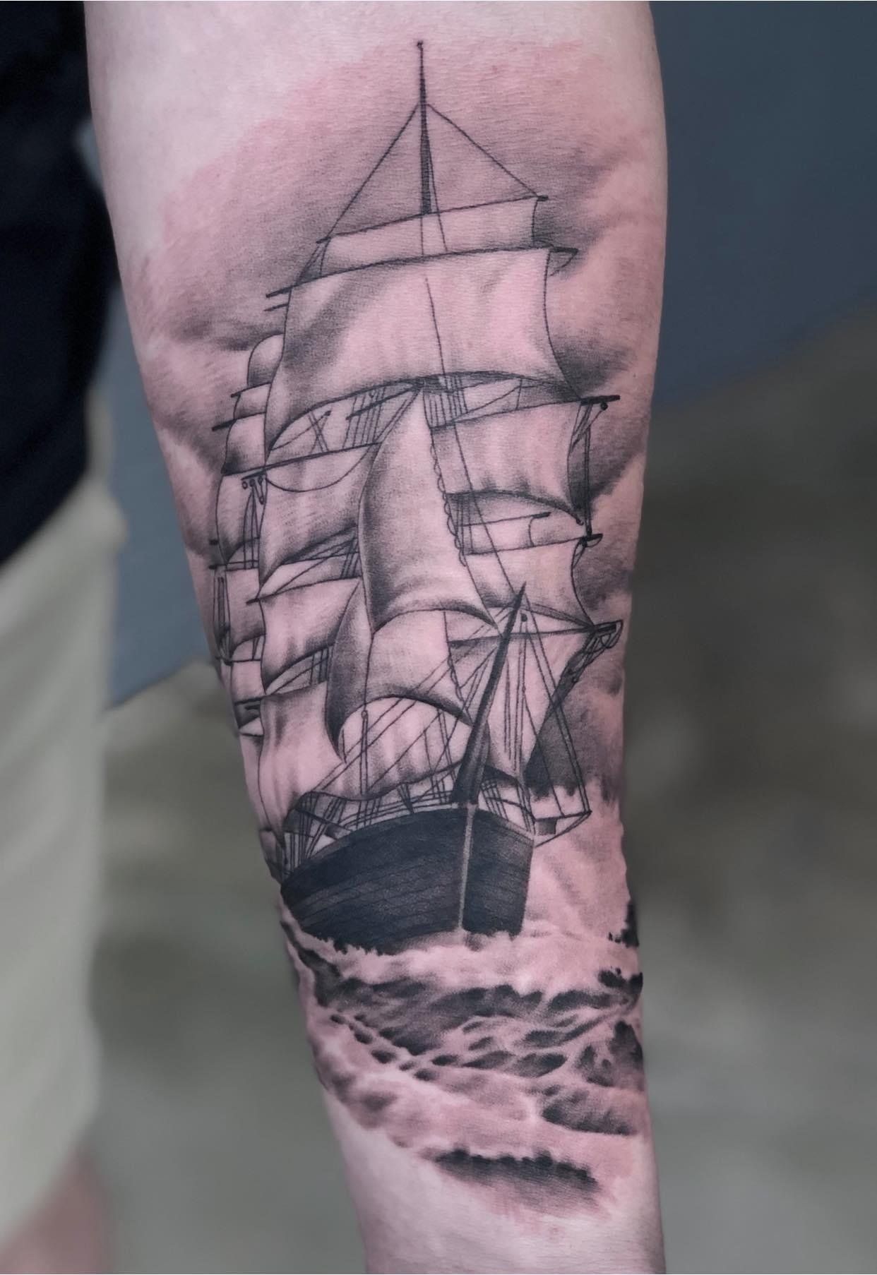 A black and white tattoo of a sailboat in the ocean on a person 's arm.