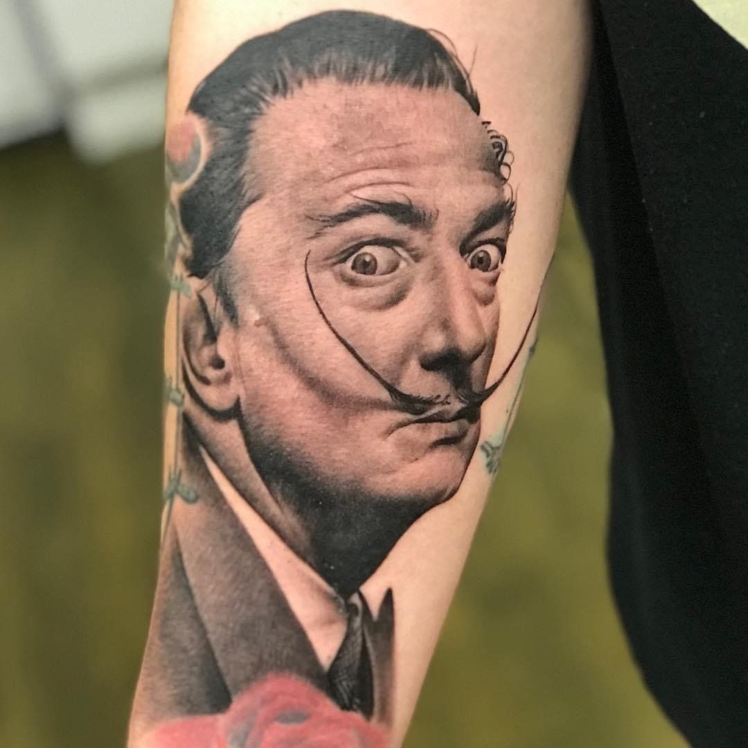 A man has a tattoo of salvador dali on his arm.