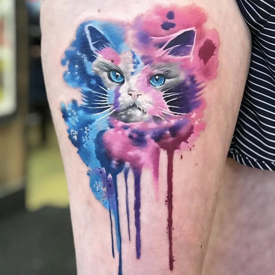 A woman has a watercolor tattoo of a cat on her leg.