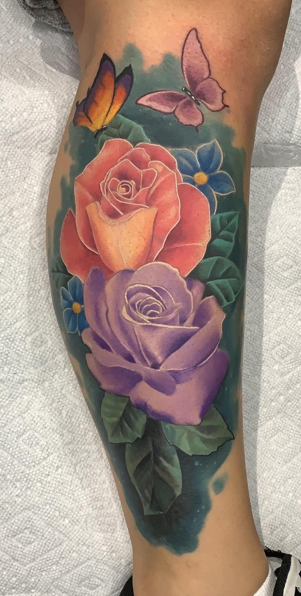 A woman has a tattoo of roses and butterflies on her leg.