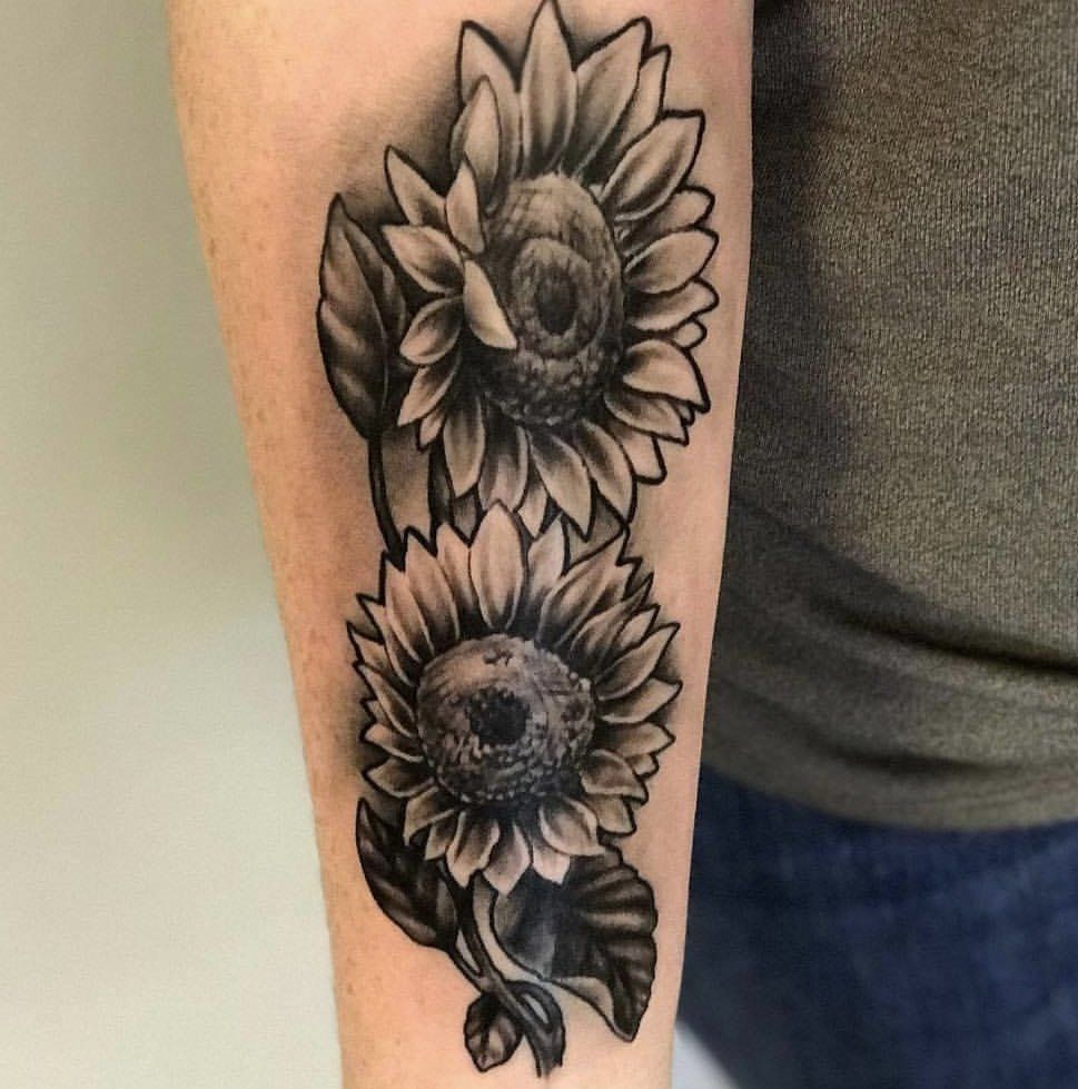 A black and white tattoo of two sunflowers on a person 's forearm.