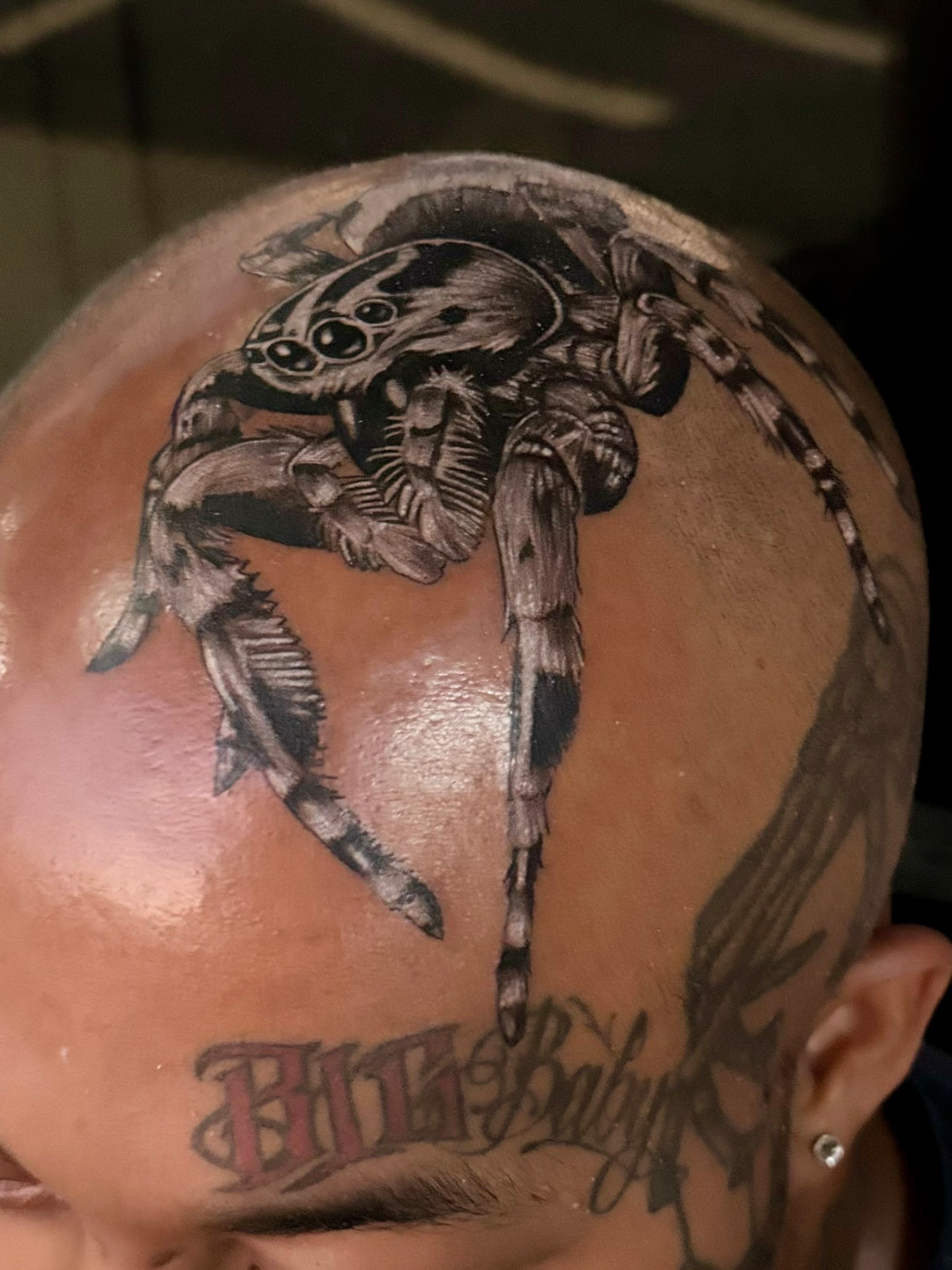 A man has a tattoo of a spider on his head.