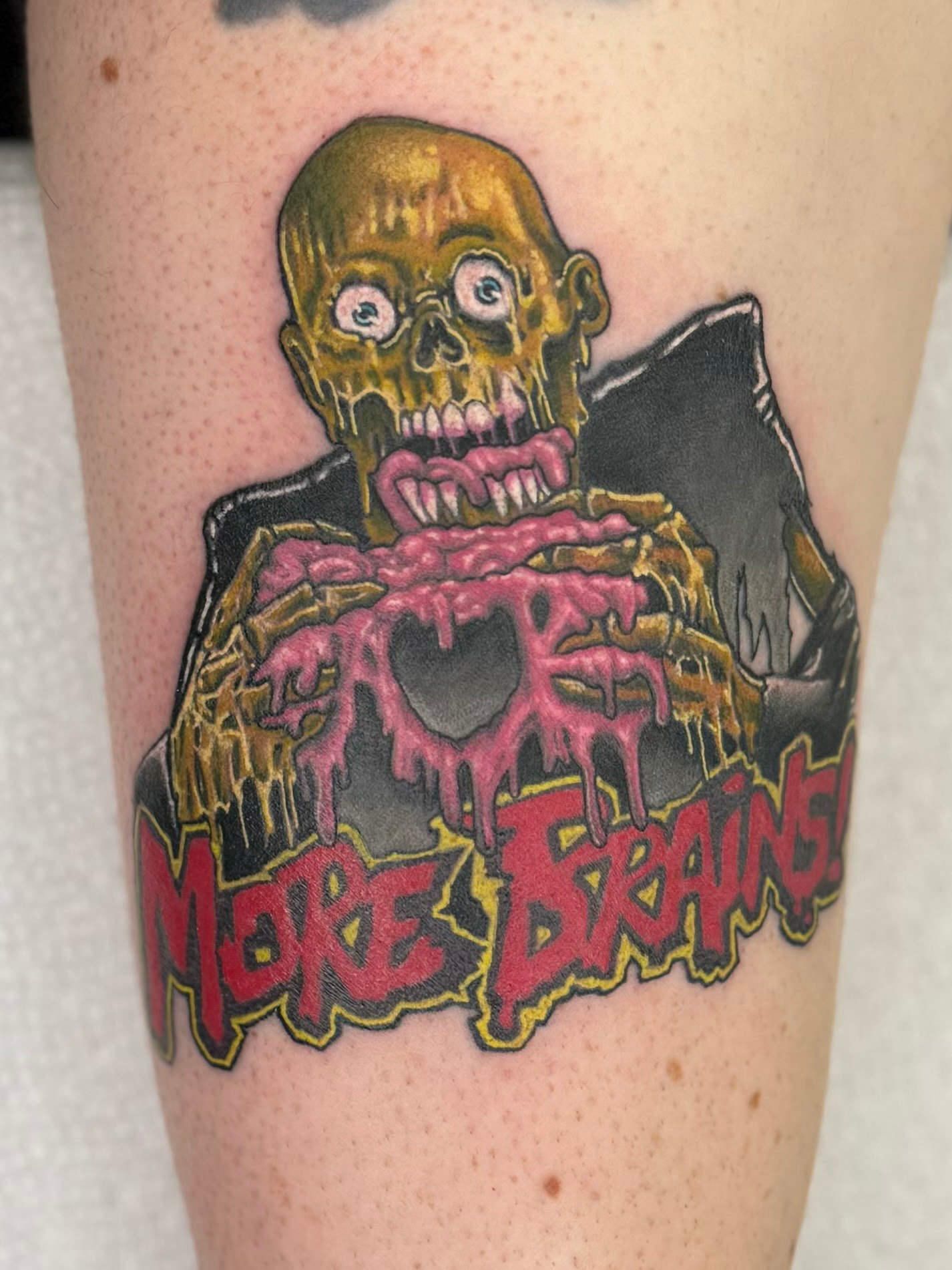 A tattoo on a person 's leg that says more brains