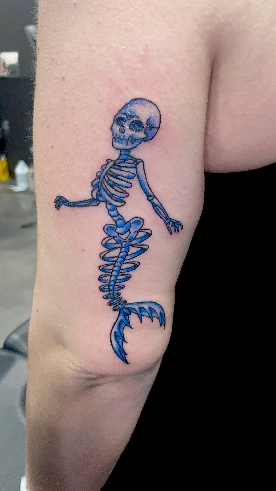 A woman has a tattoo of a skeleton mermaid on her arm