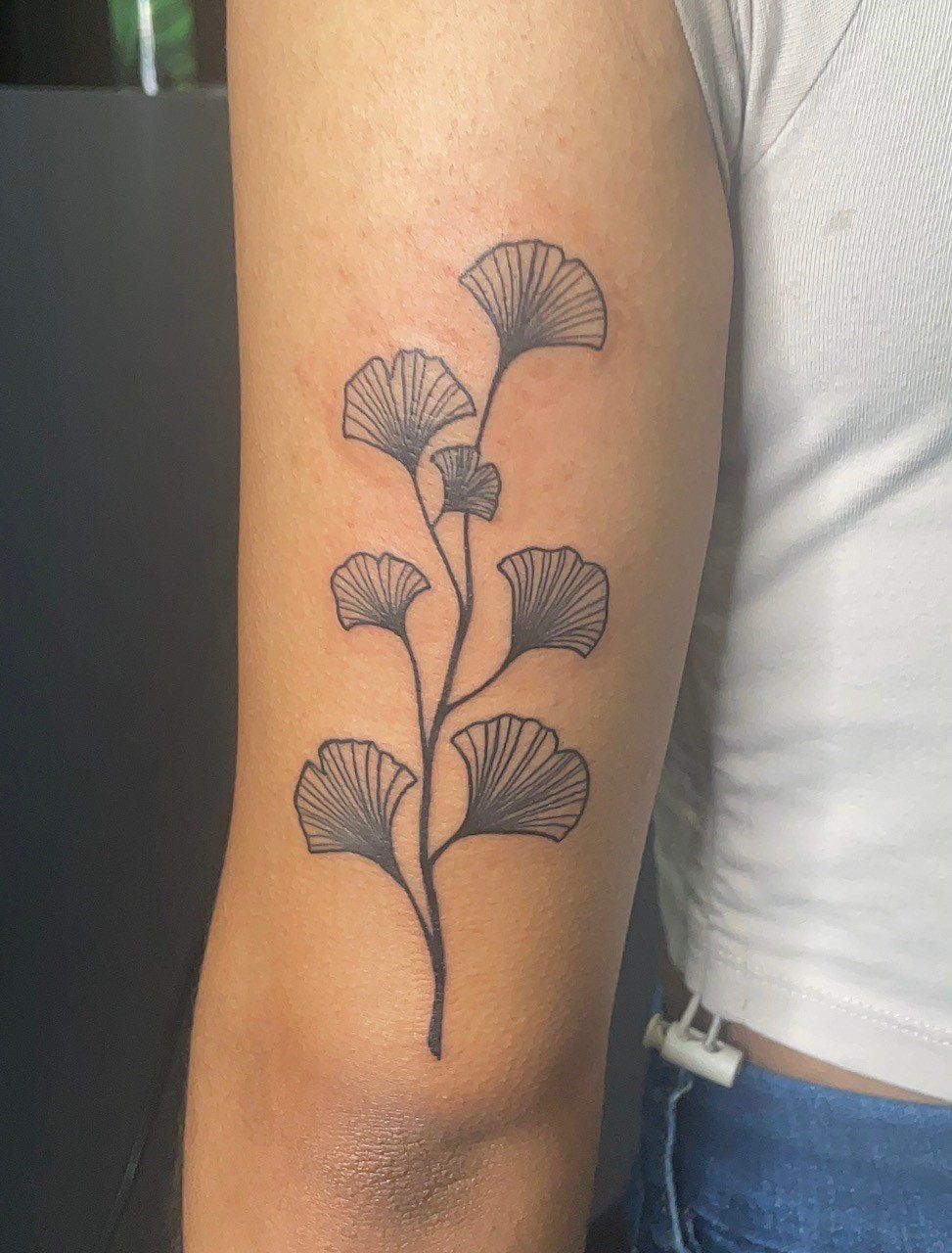 A woman has a tattoo of a branch with leaves on her arm.