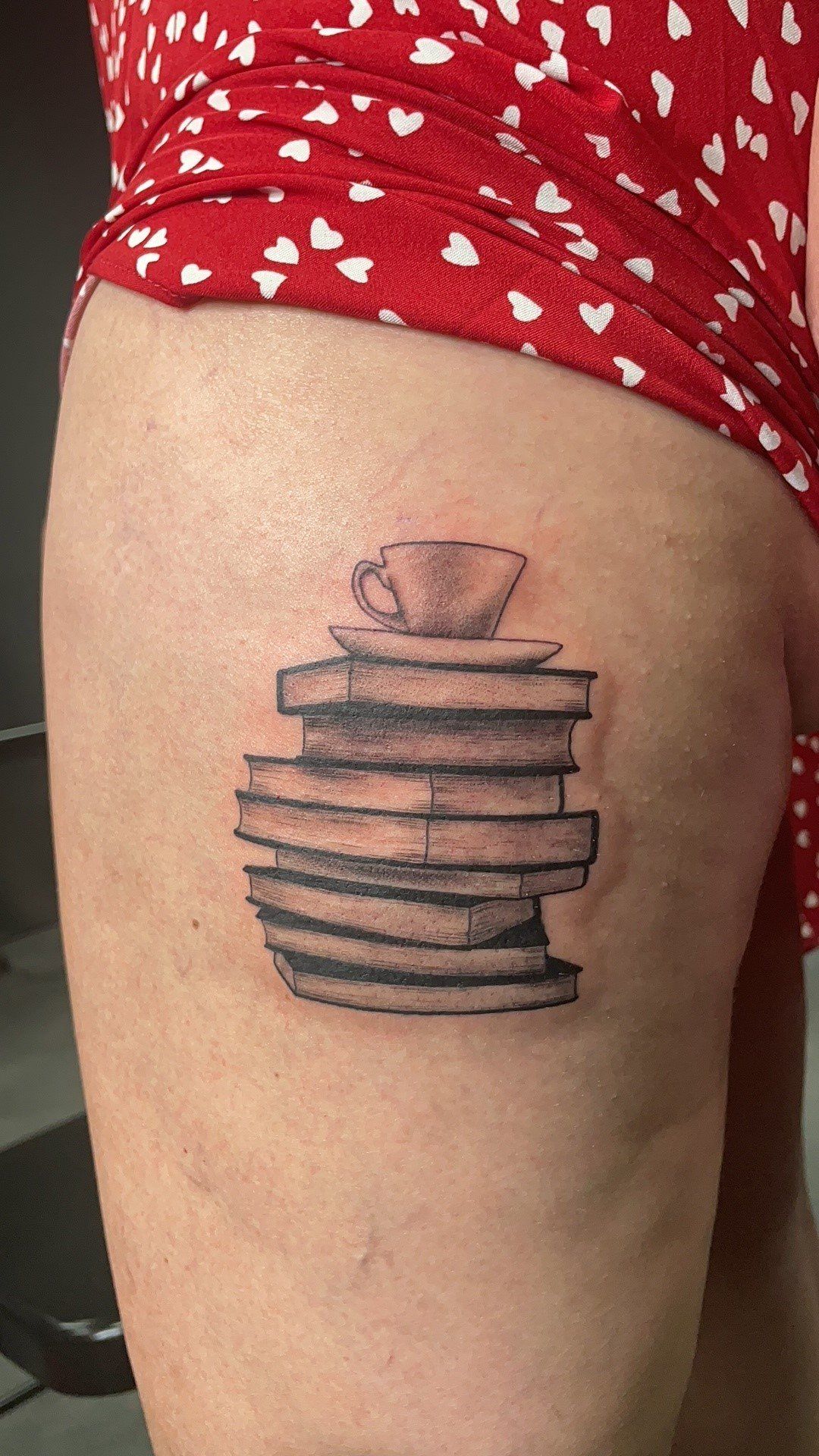 A woman has a tattoo of a stack of books and a cup of coffee on her leg.