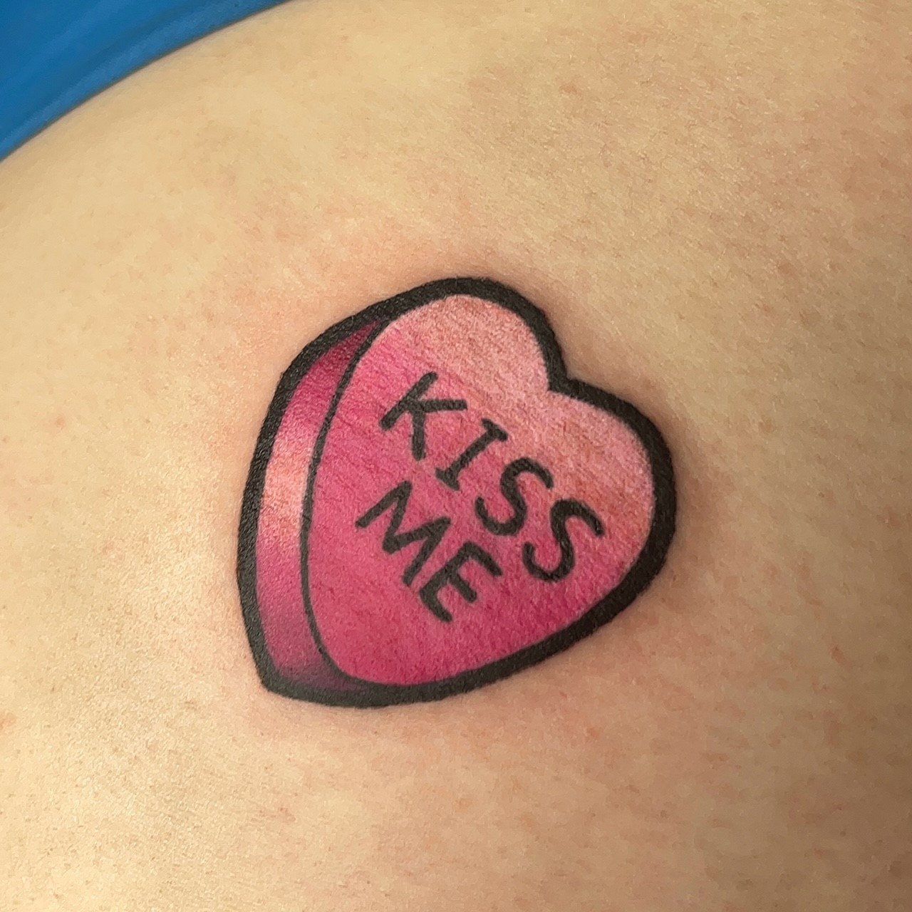 A tattoo of a candy heart that says kiss me