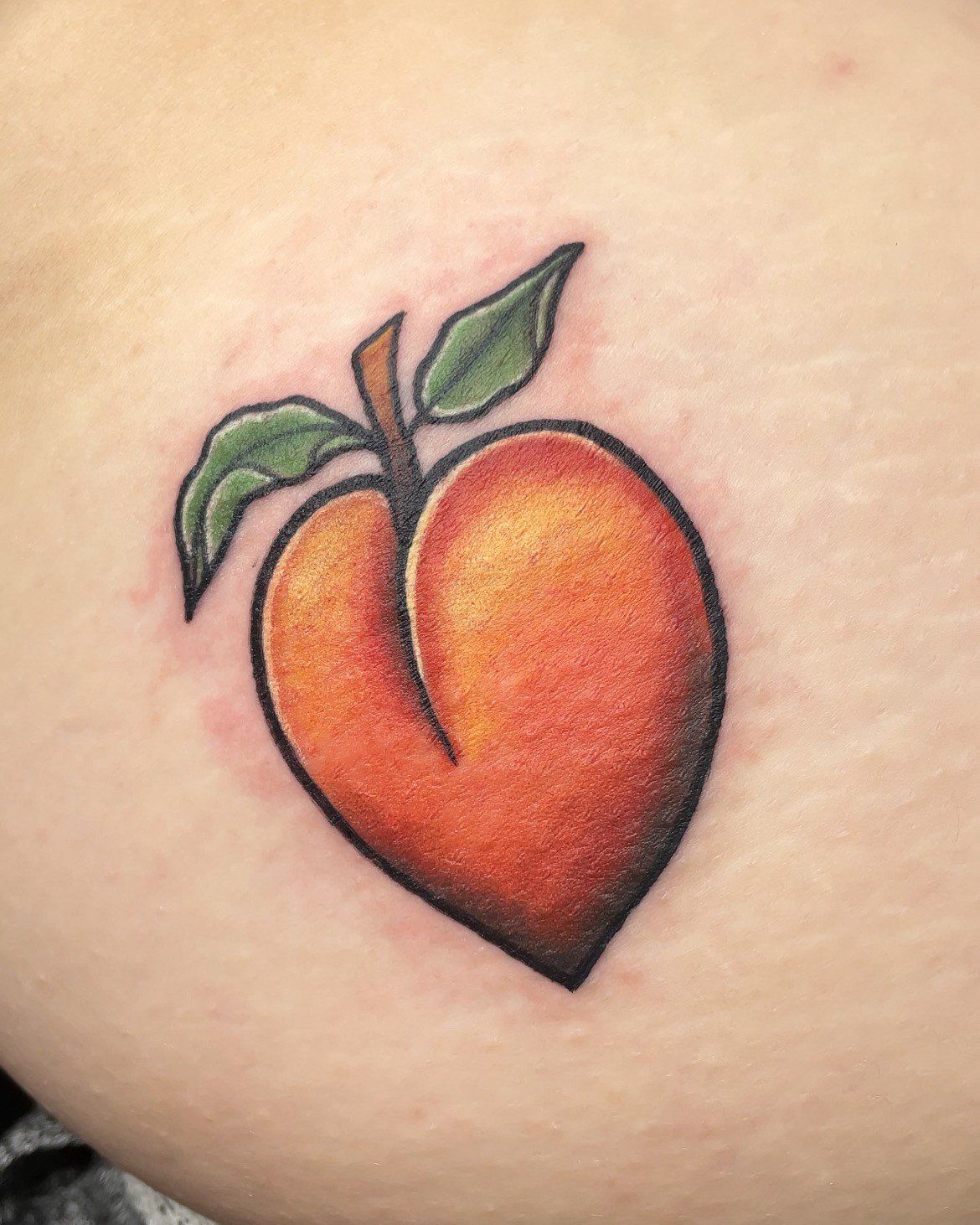 A close up of a tattoo of a peach on a person 's leg.