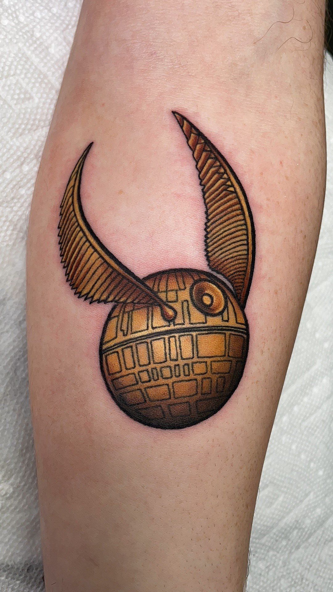 A tattoo of a golden snitch from harry potter on a person 's leg.