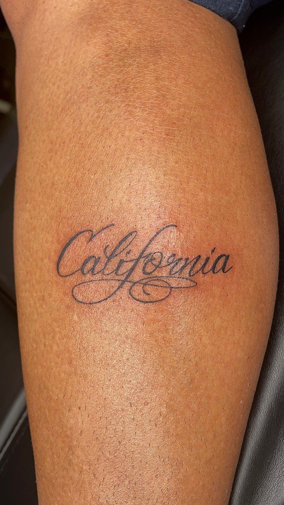 A person has a tattoo of the word california on their leg.