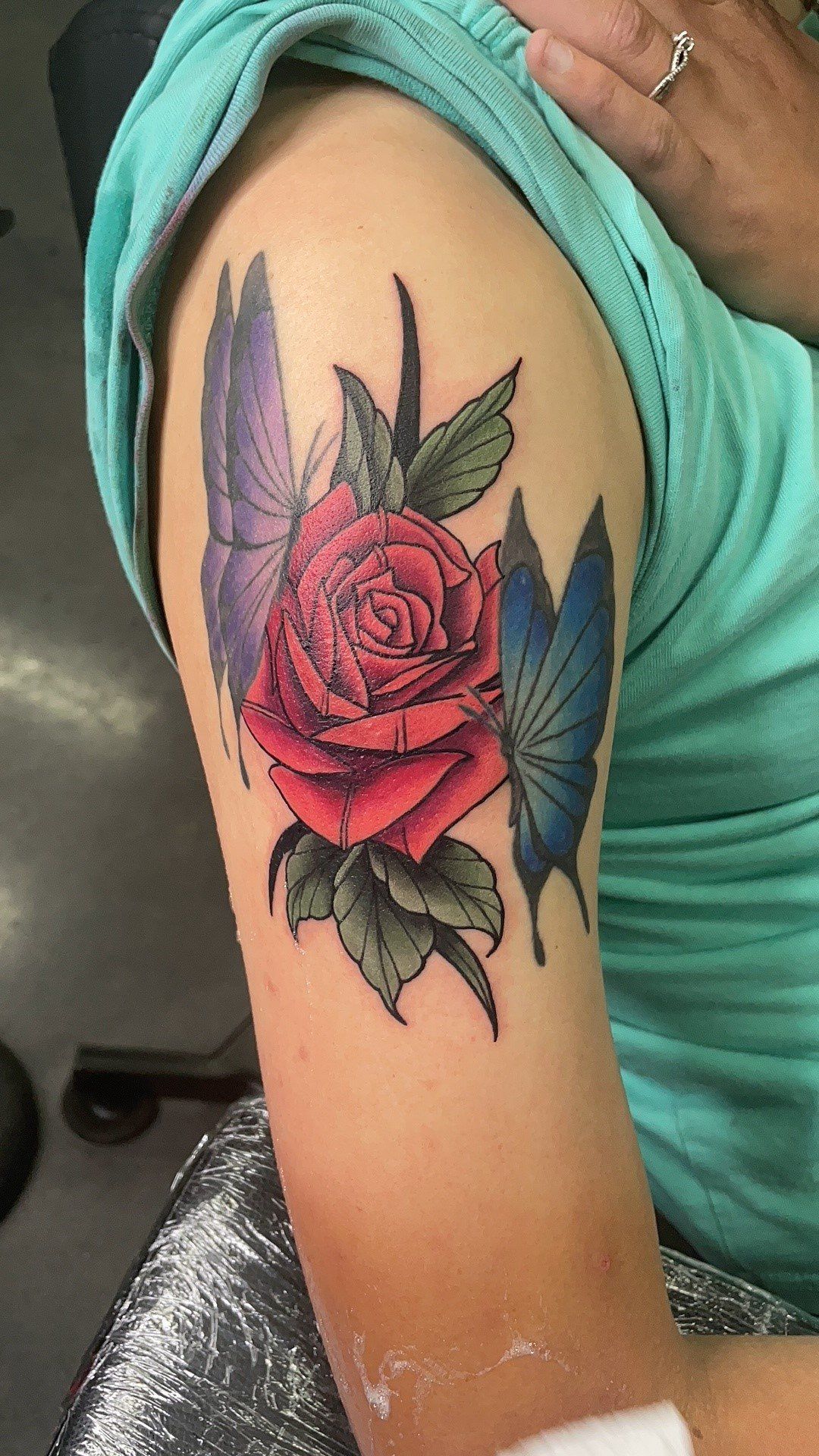 A woman has a tattoo of a rose and butterflies on her arm.
