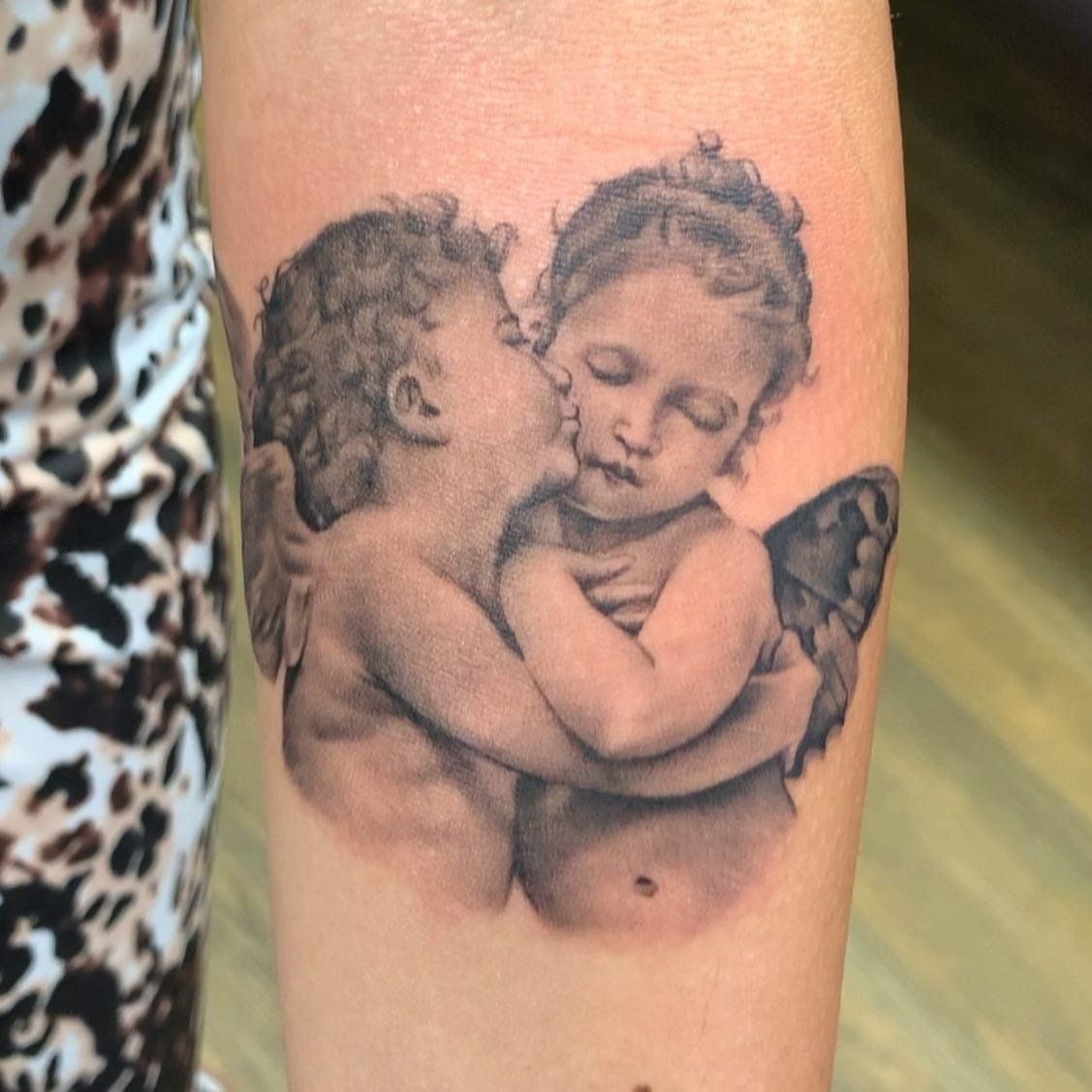 A tattoo of two cherubs hugging each other on a woman 's arm
