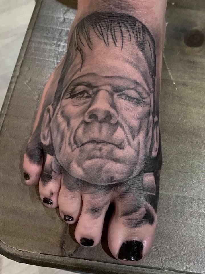 A black and white tattoo of frankenstein 's head on a foot.