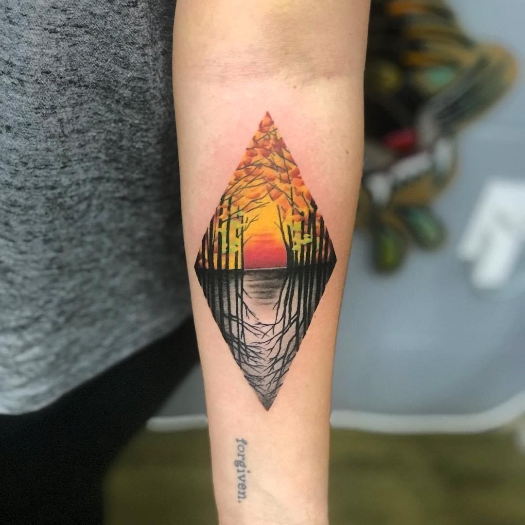A person has a tattoo of a sunset in a diamond shape on their forearm