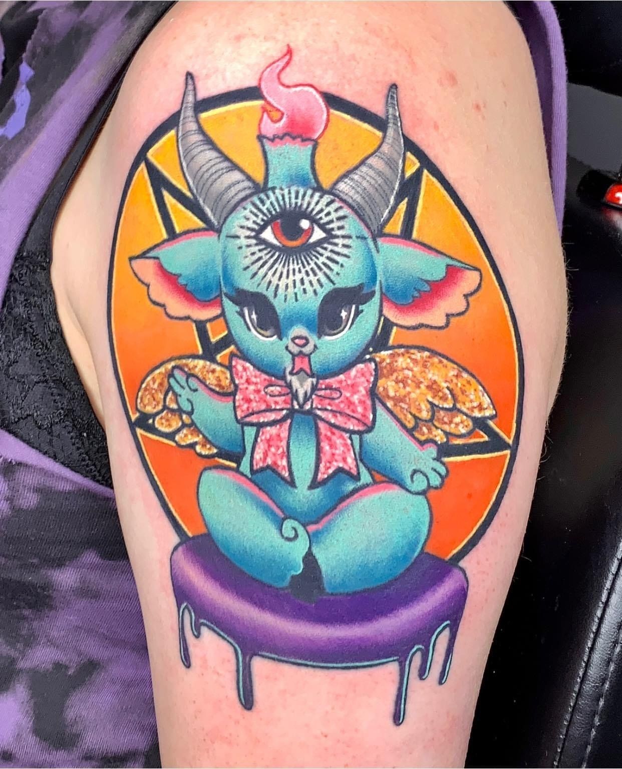 A person has a tattoo of a gremlin with horns on their arm