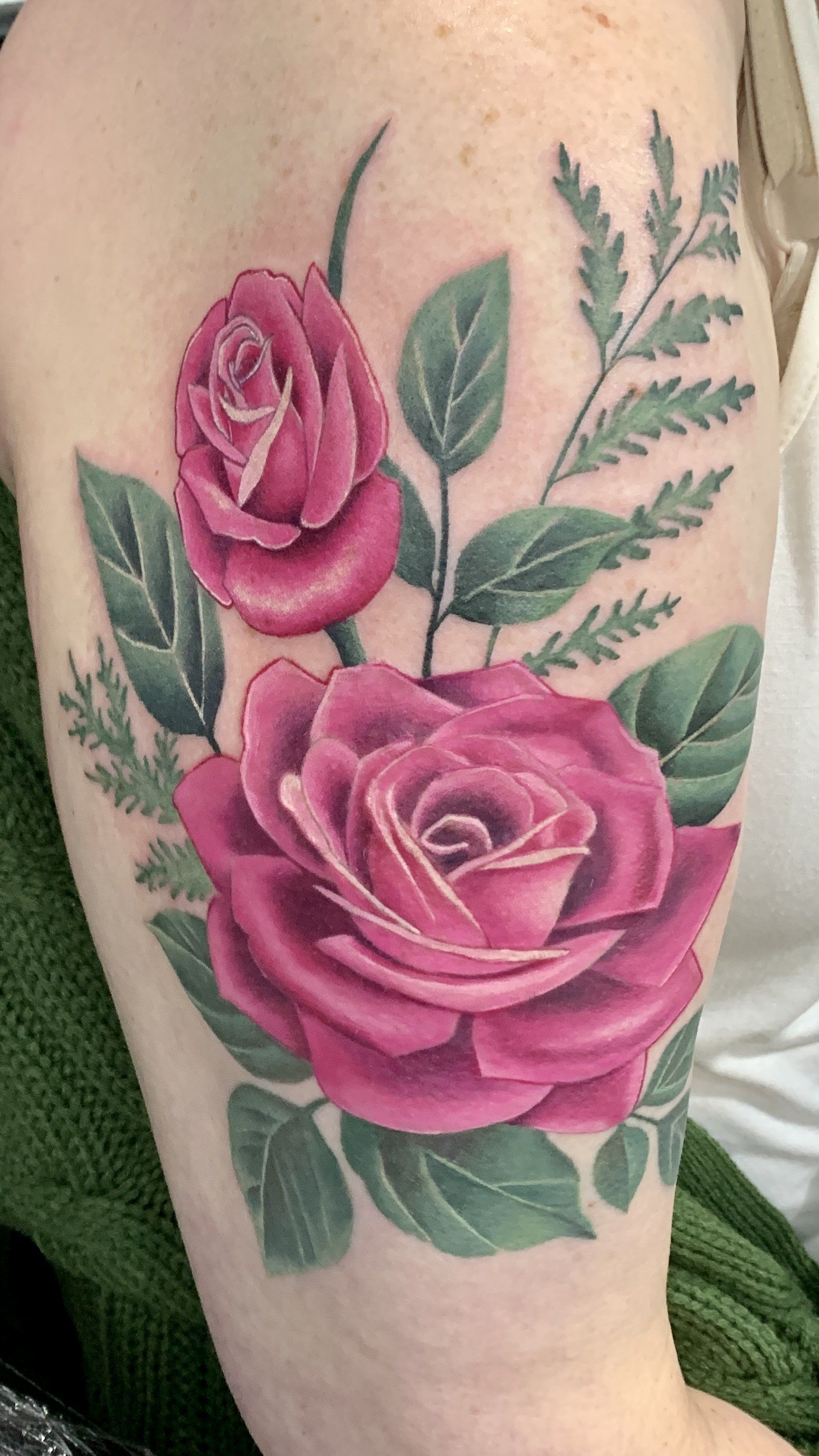 A woman has a tattoo of pink roses and green leaves on her arm.