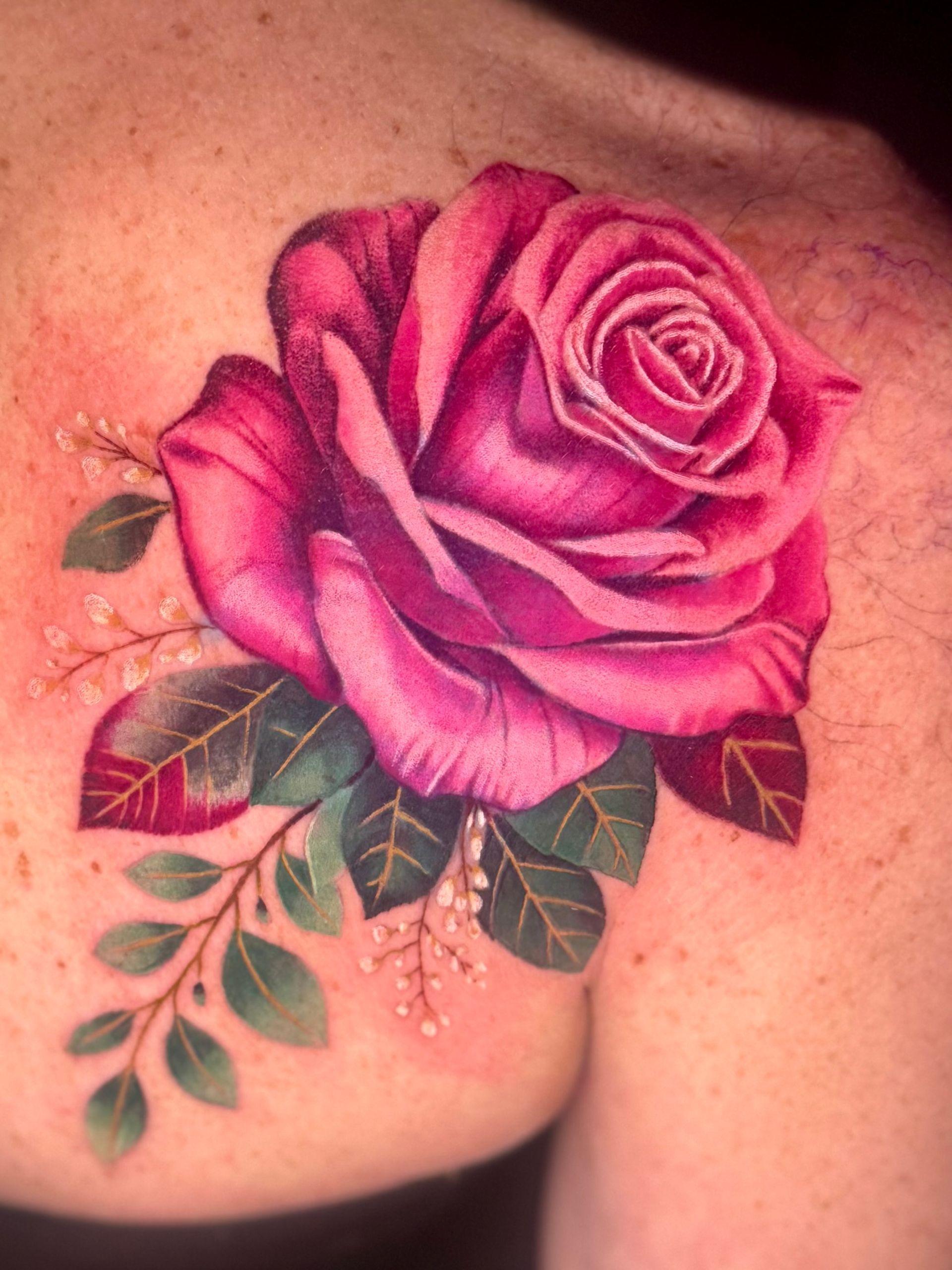 Pink rose tattoo with green leaves on skin