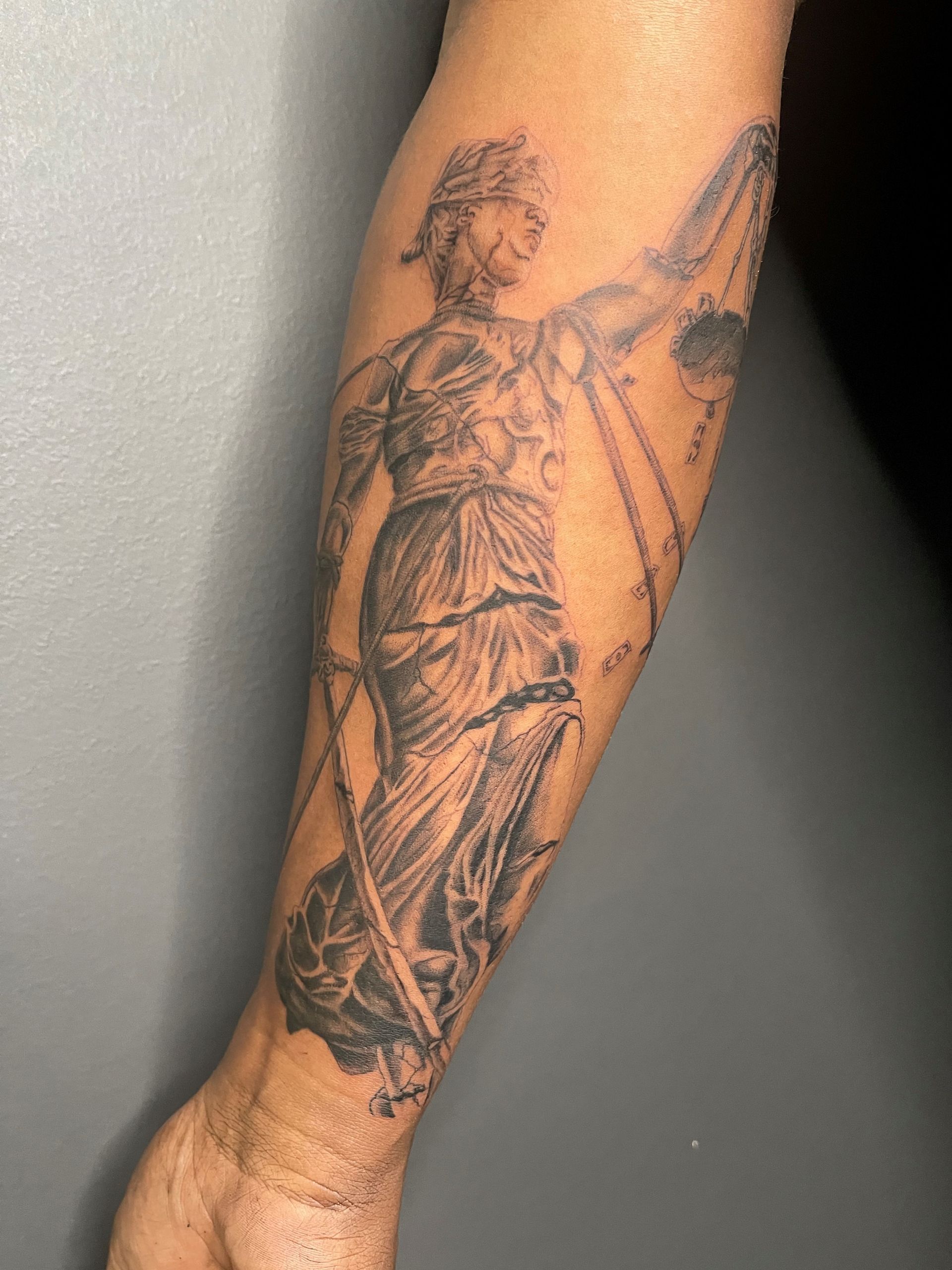 A person has a tattoo of a statue of justice on their arm.