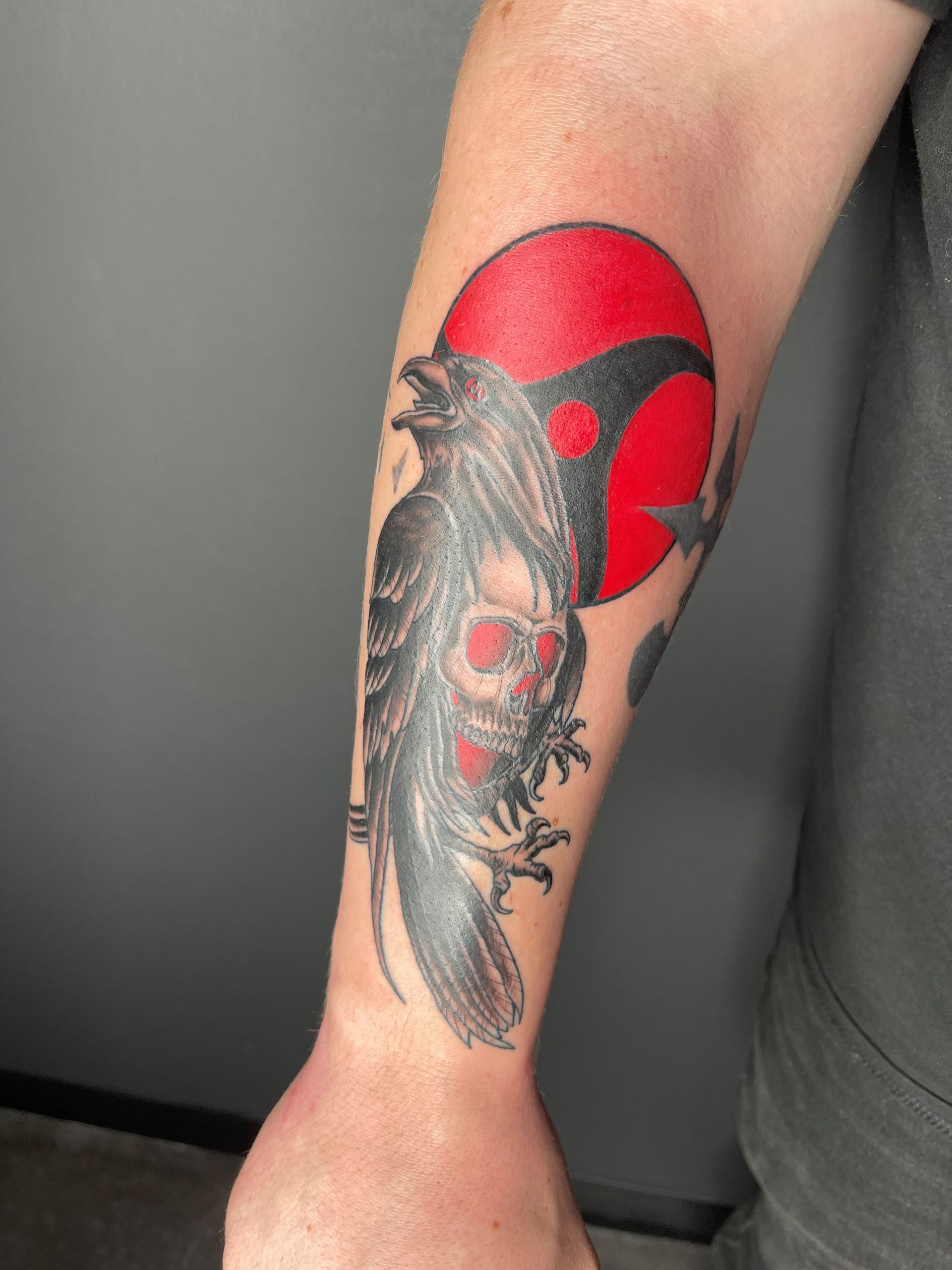 A person has a tattoo of a bird and a red sun on their arm.