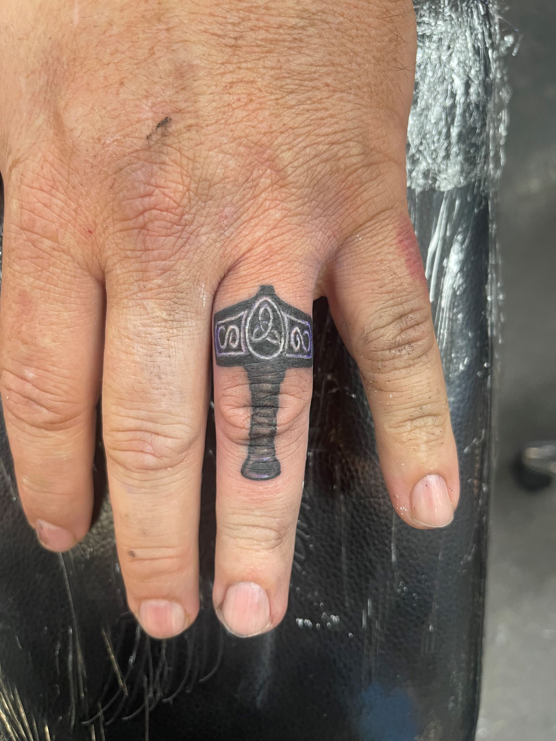 A person has a tattoo of a hammer on their finger.