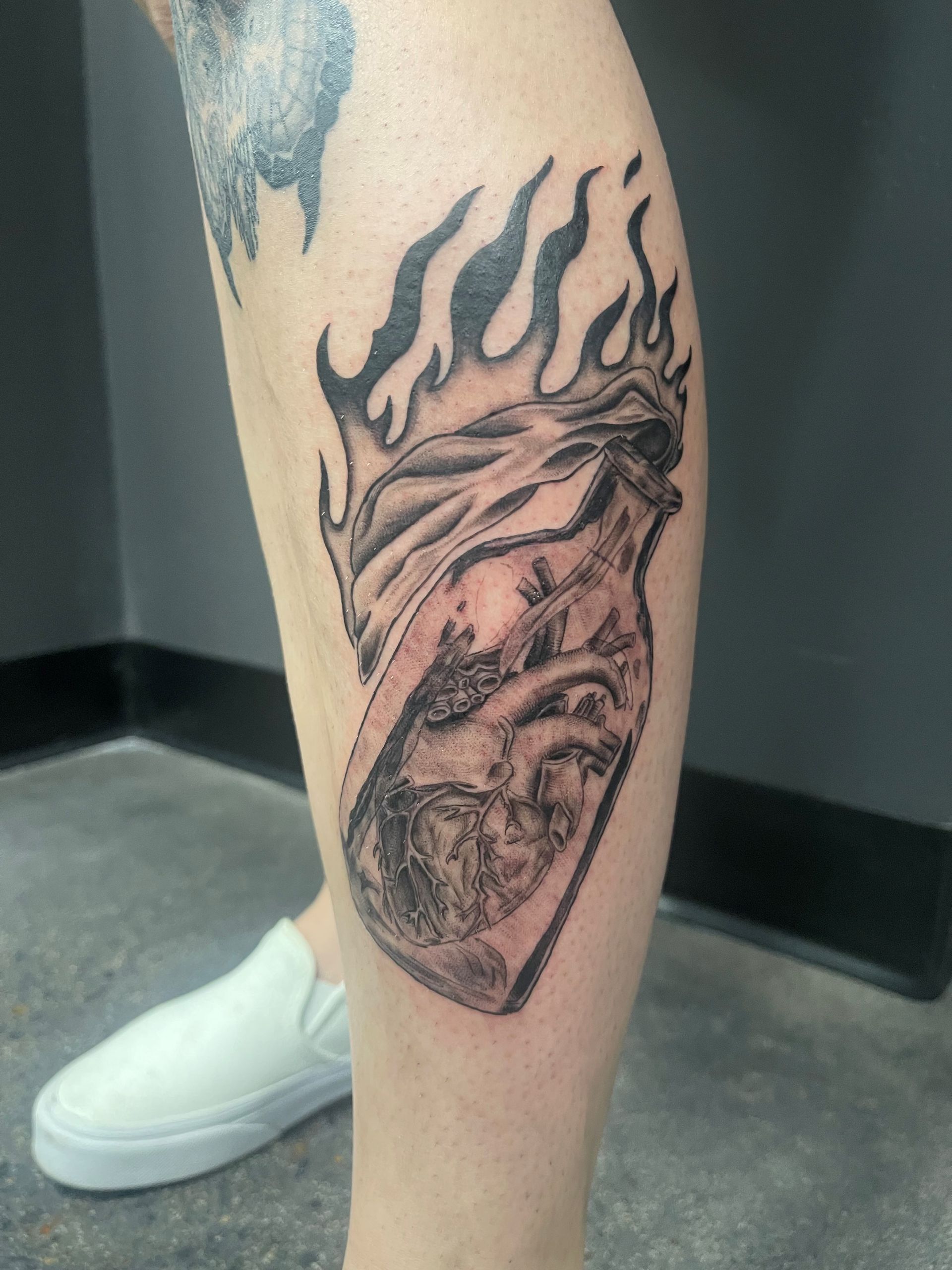 A person has a tattoo of a heart with flames on their leg.