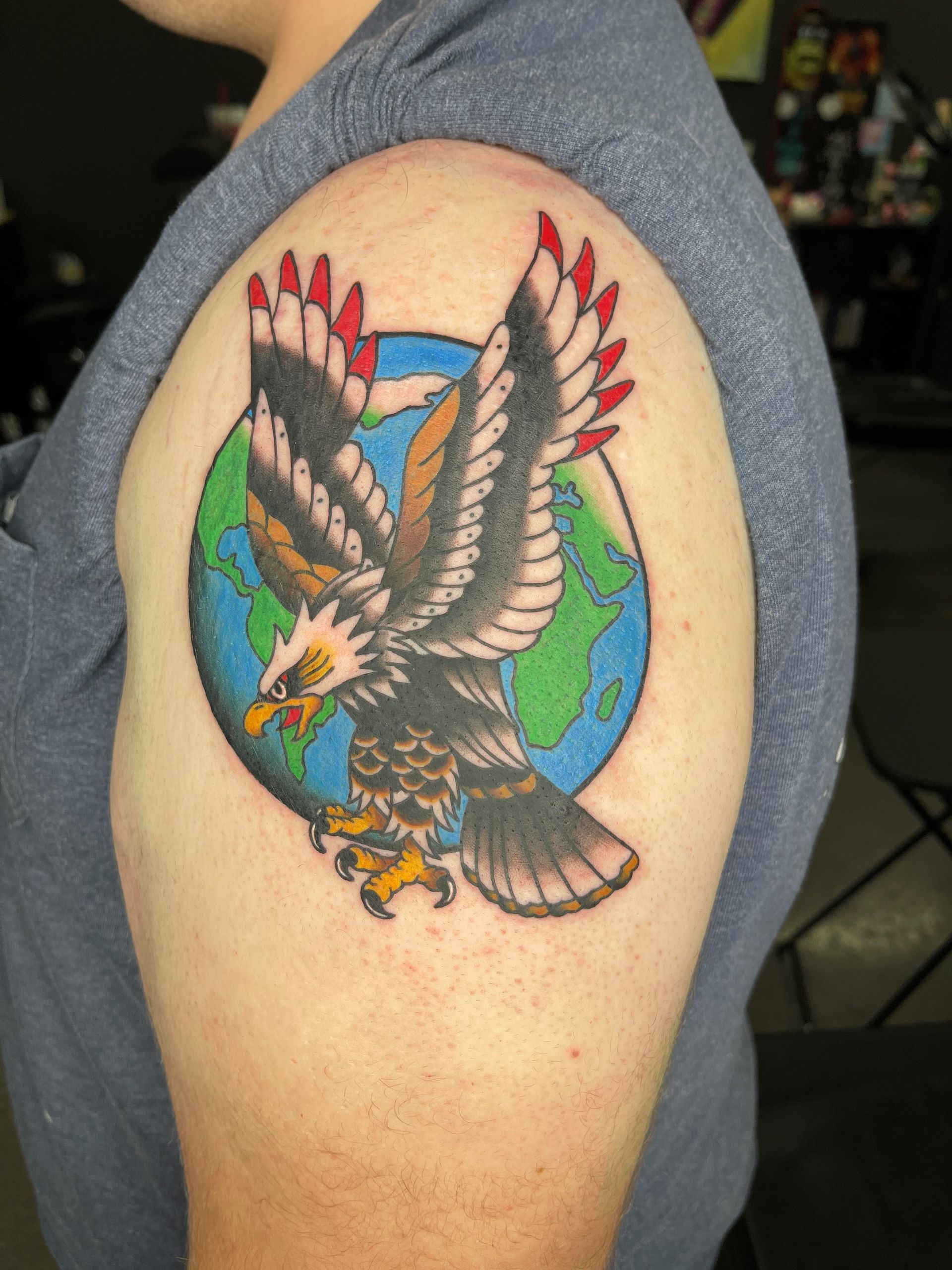 A man has a tattoo of an eagle flying over a globe