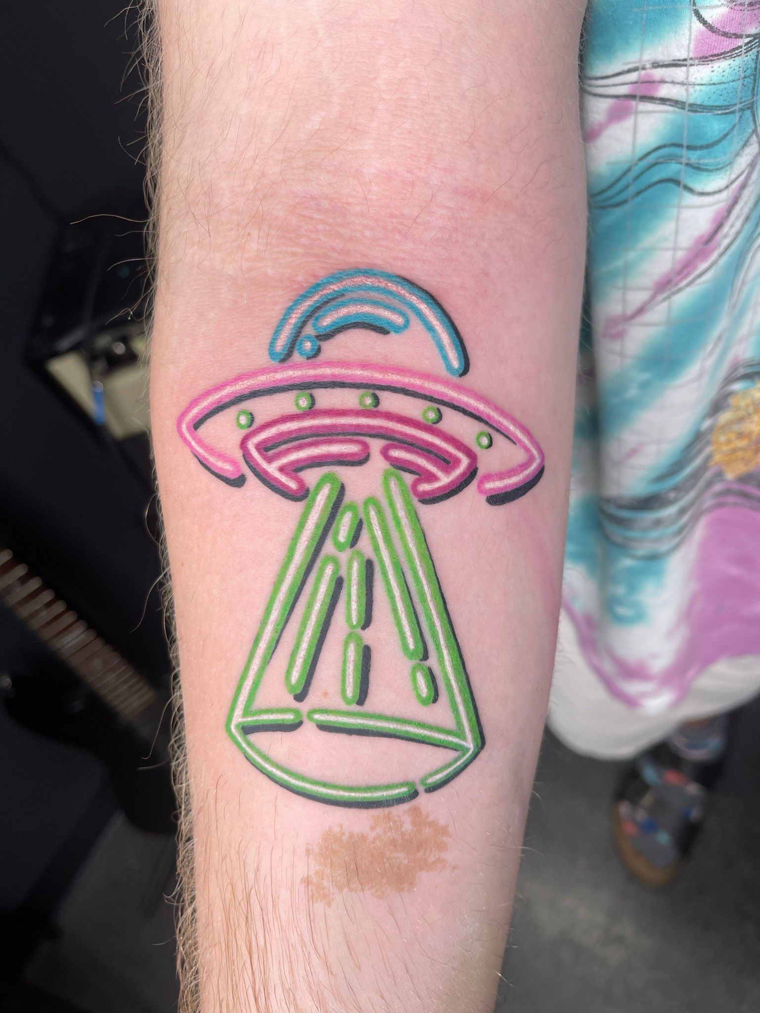 A person has a neon alien tattoo on their forearm.