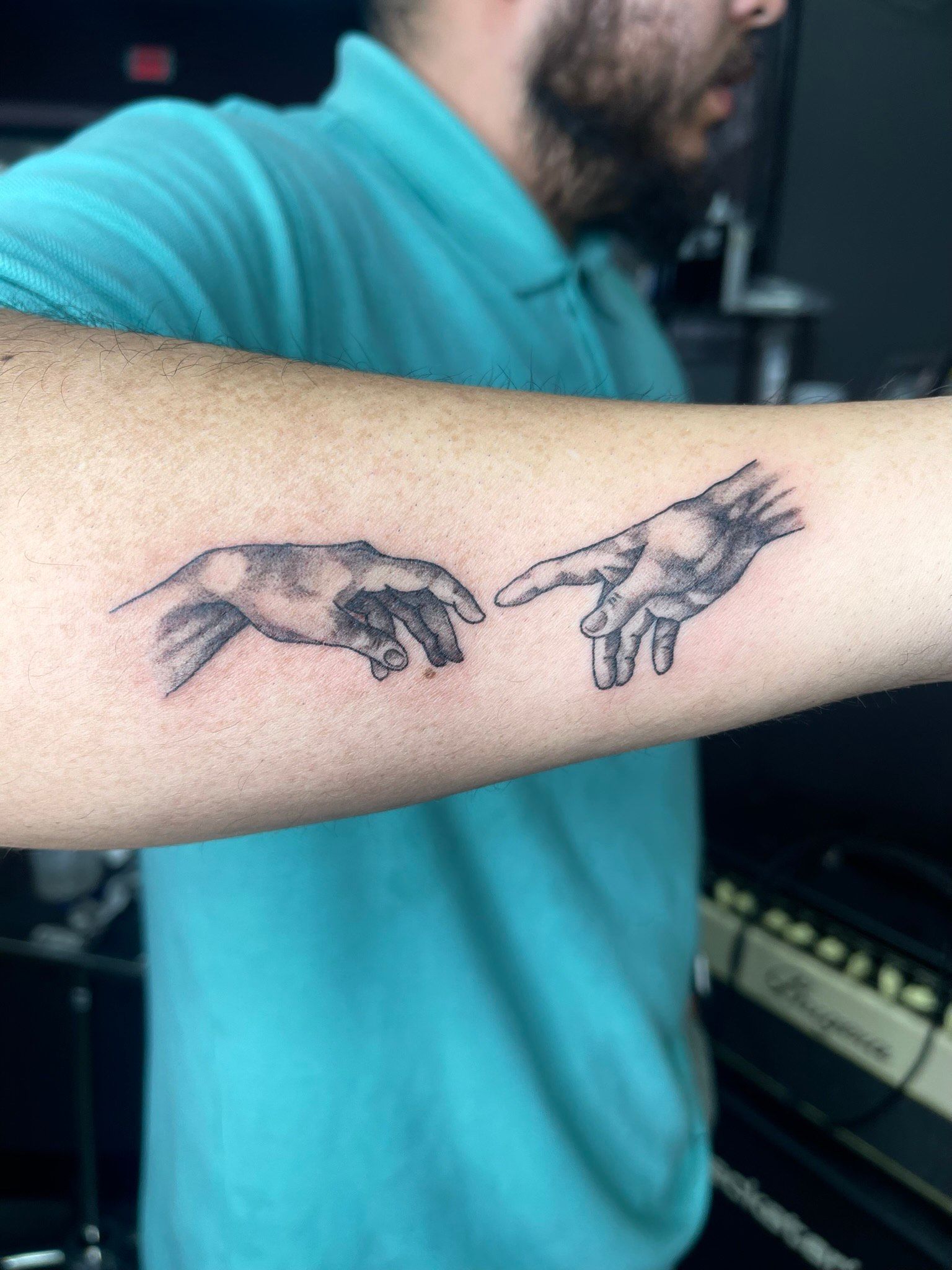 A man has a tattoo of the creation of adam on his forearm.